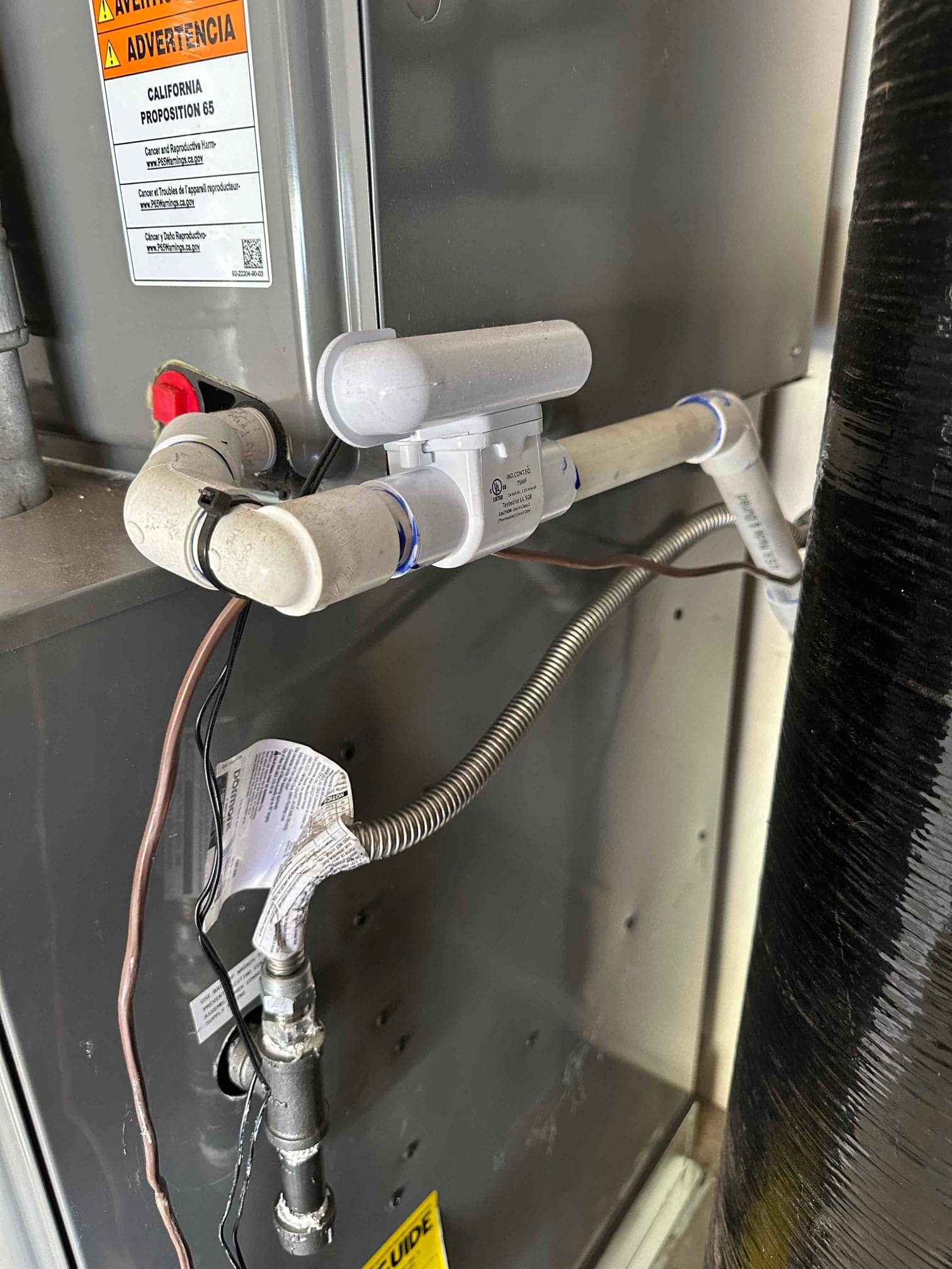 Condensate drain with float switch installed on the furnace cabinet, alongside gas flex connector and wiring secured to the housing.