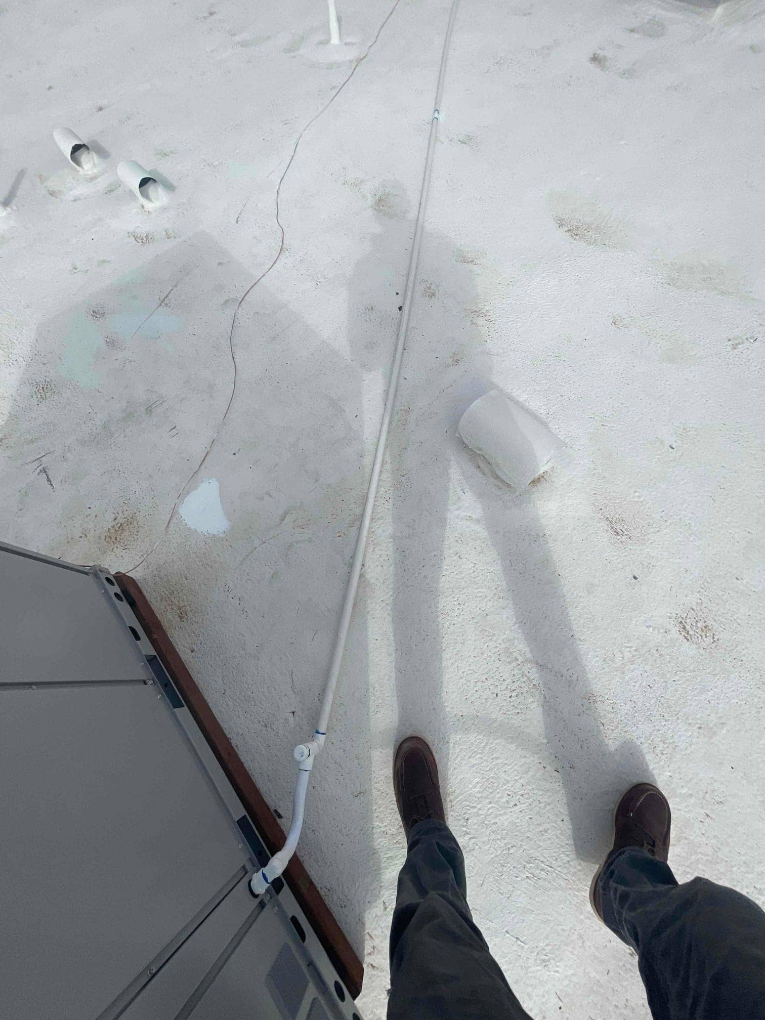 Condensate drain line routed from rooftop condenser across the roof surface with fittings and supports visible.