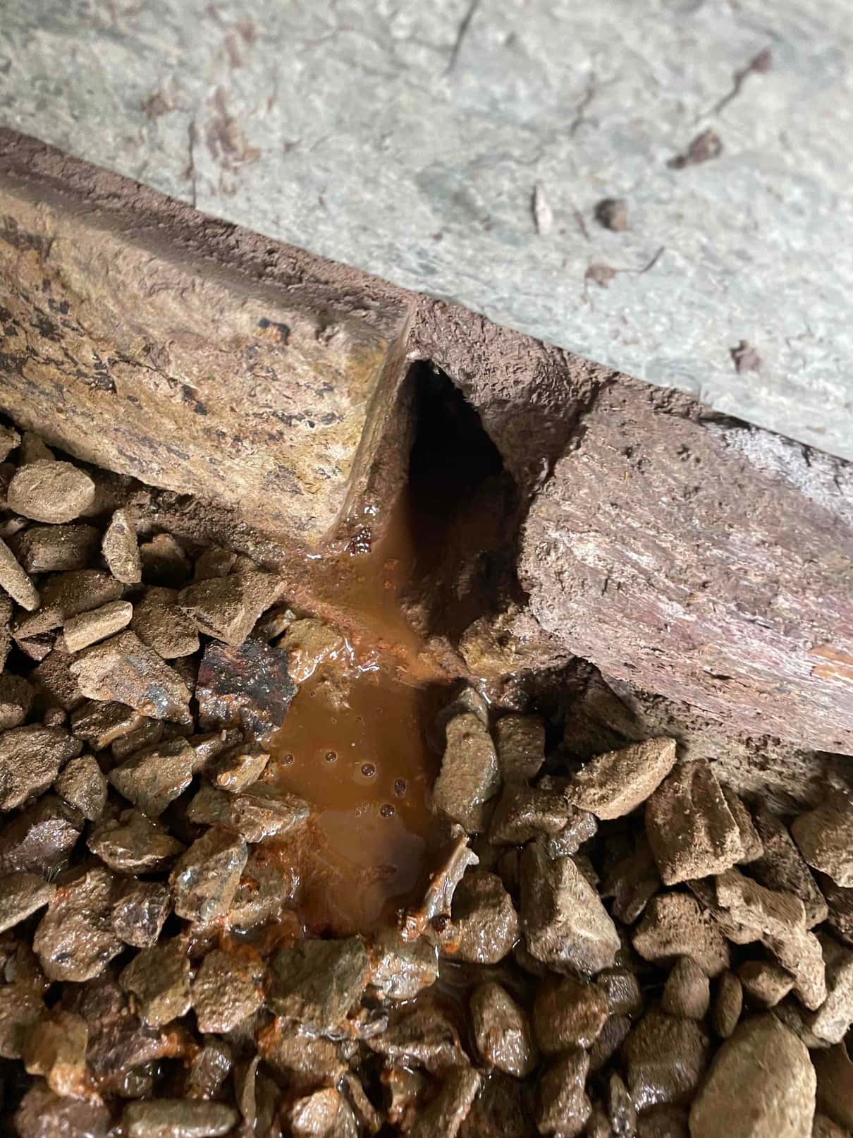 Condensate drain outlet discharging rusty water onto gravel at the installation site, showing drainage path outside the structure.