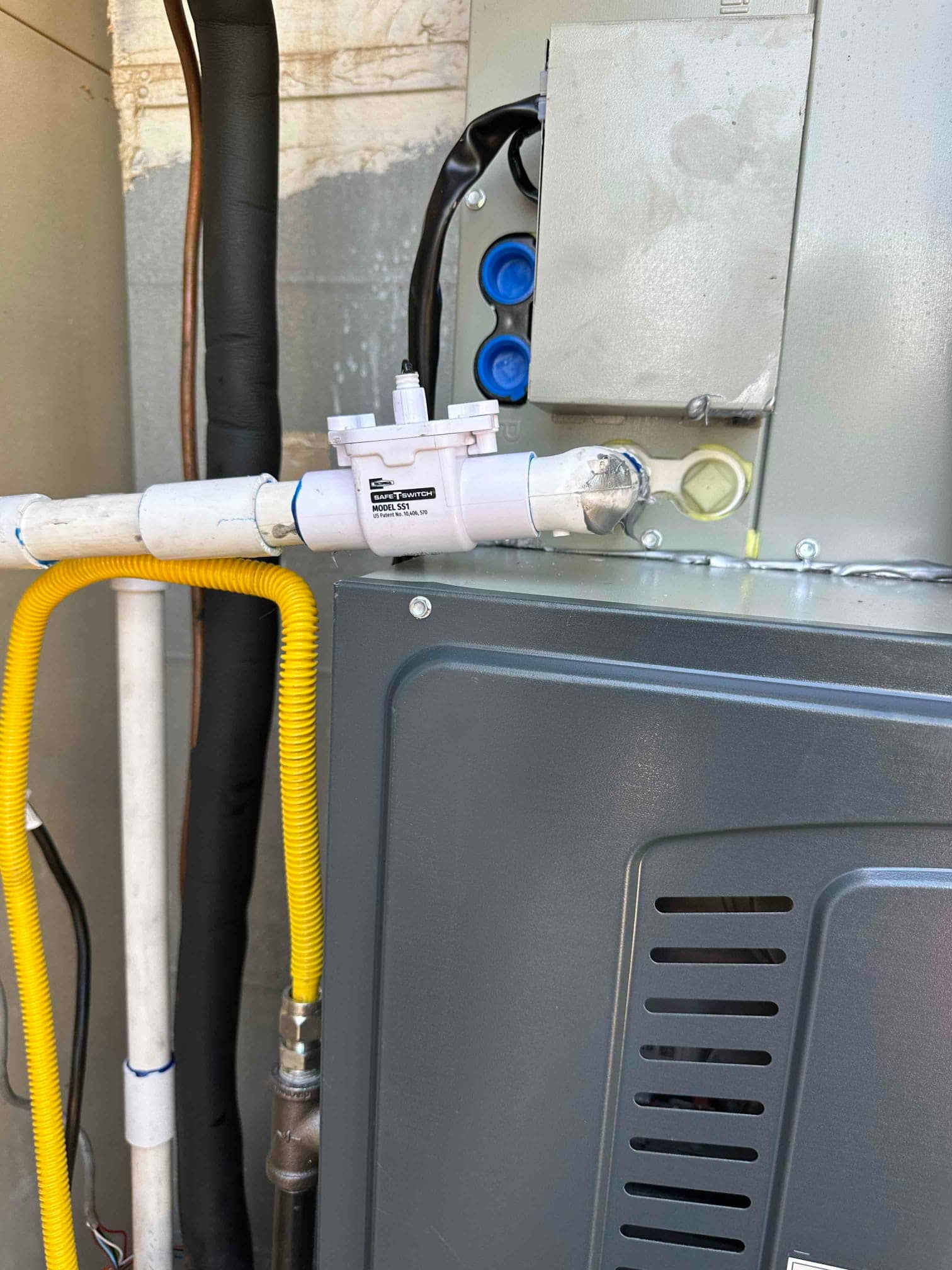 Condensate safety switch installed on the drain line beside the furnace with gas flex connector and insulated refrigerant lines.