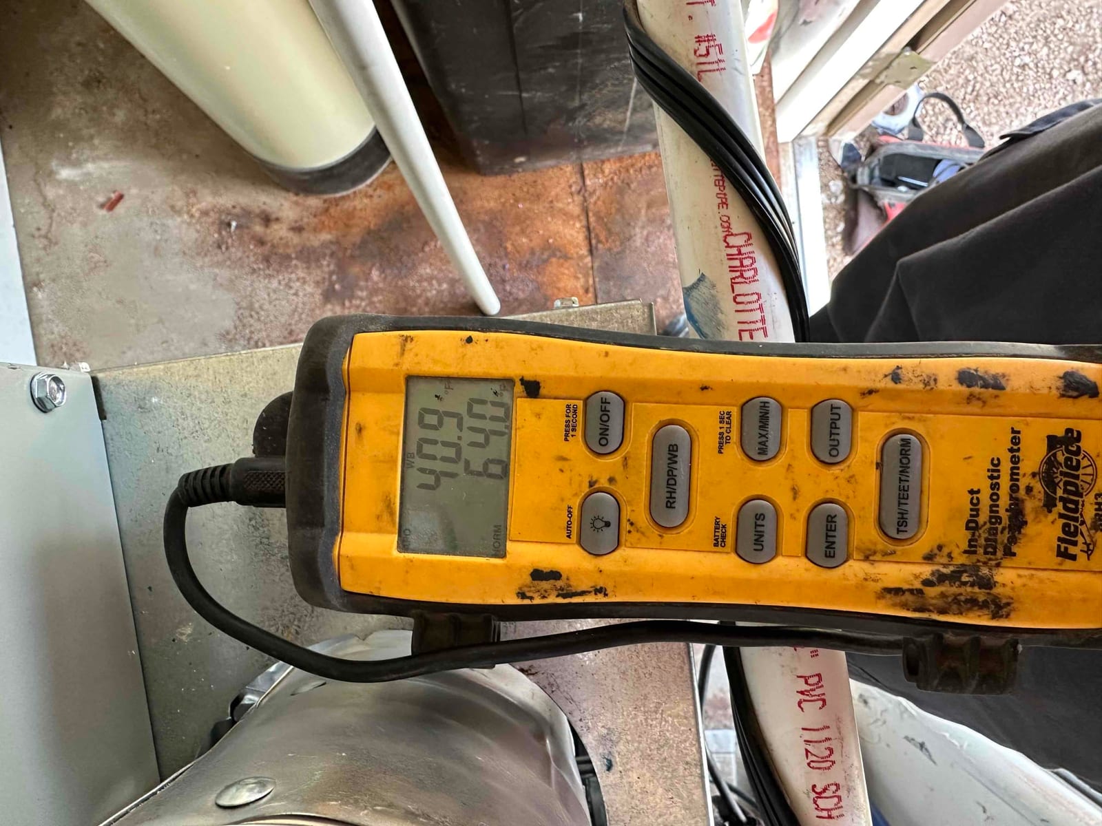 Digital duct thermometer placed at the air handler shows a temperature reading on the display during airflow verification.