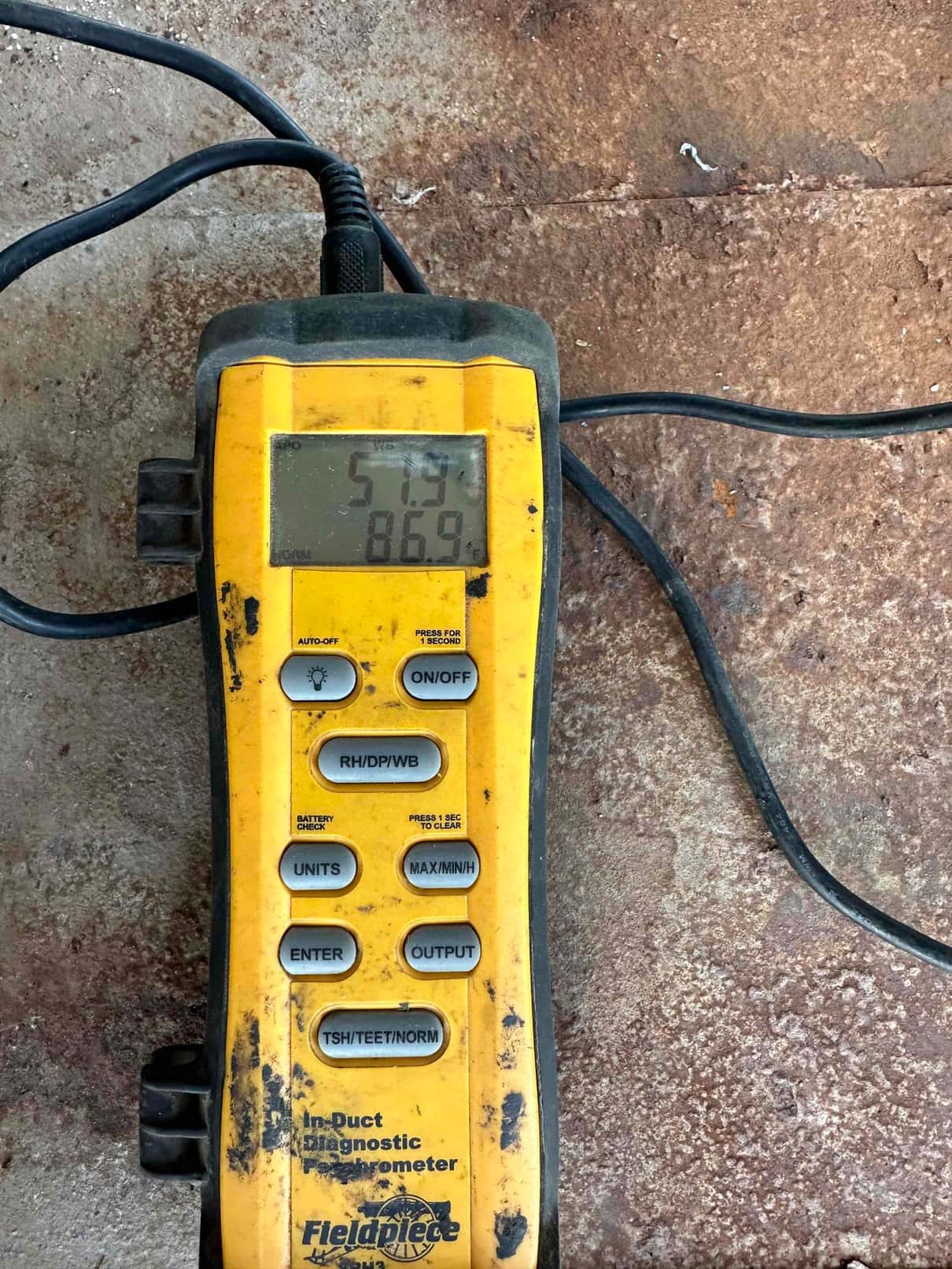 Digital in-duct thermometer shows 57.9 degrees on the upper display and 86.9 on the lower display during airflow testing.