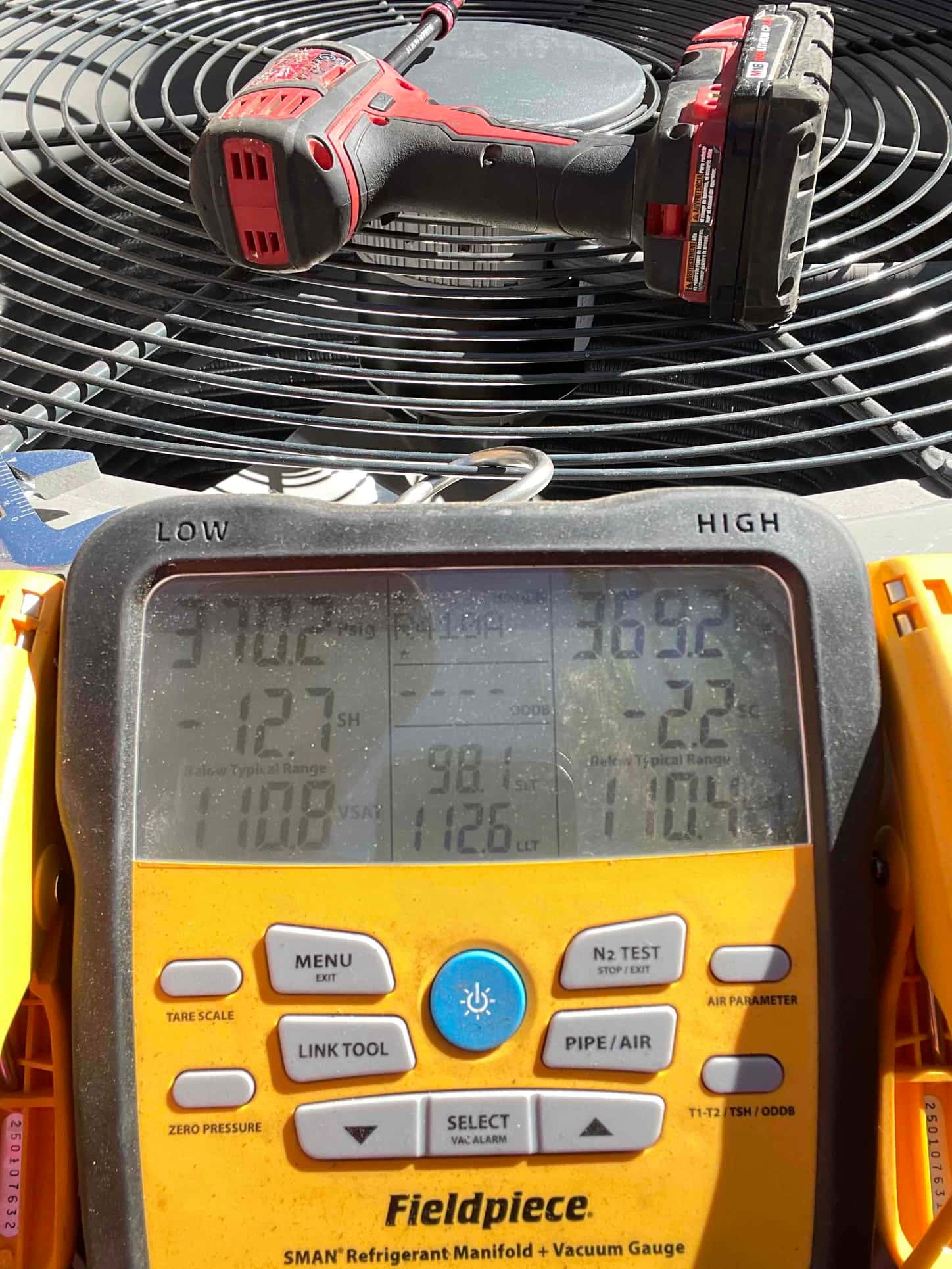 Digital manifold connected to the outdoor unit shows operating pressures with split high and low sides during refrigerant commissioning.