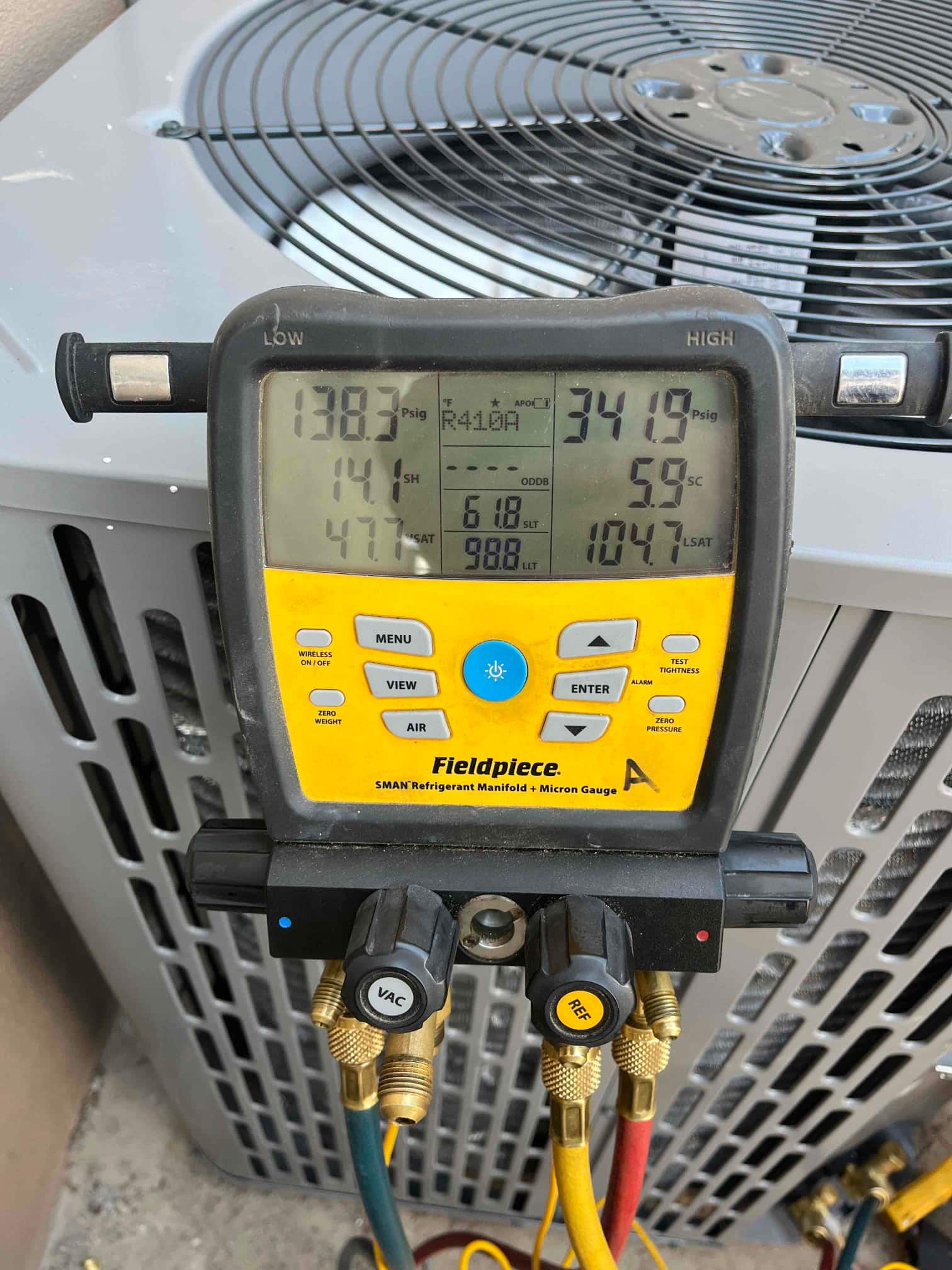 Digital manifold connected at the outdoor unit shows operating pressures while the air conditioner runs on R‑410A refrigerant.