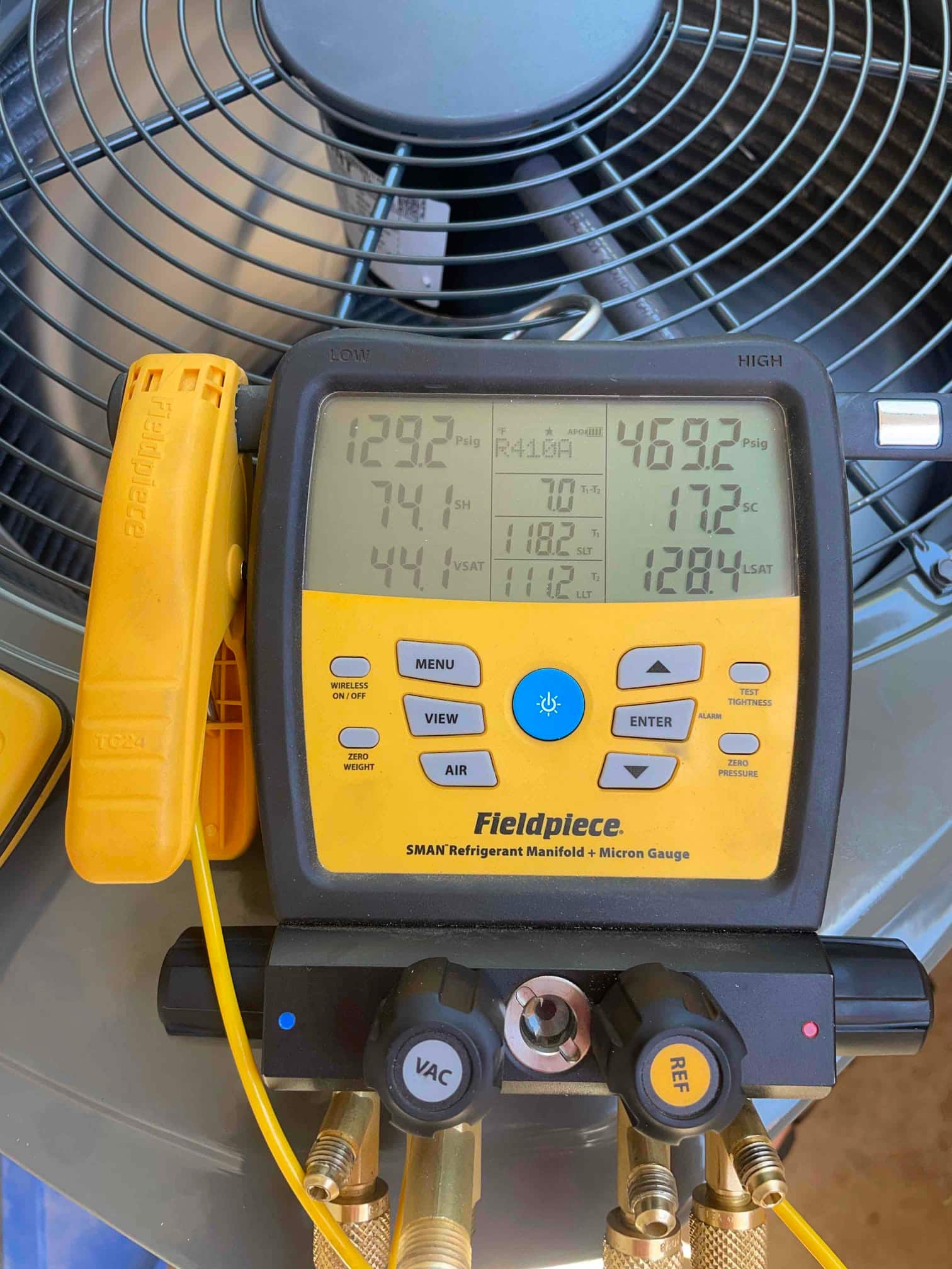 Digital manifold on the outdoor condenser shows operating pressures with superheat and subcooling during system commissioning.