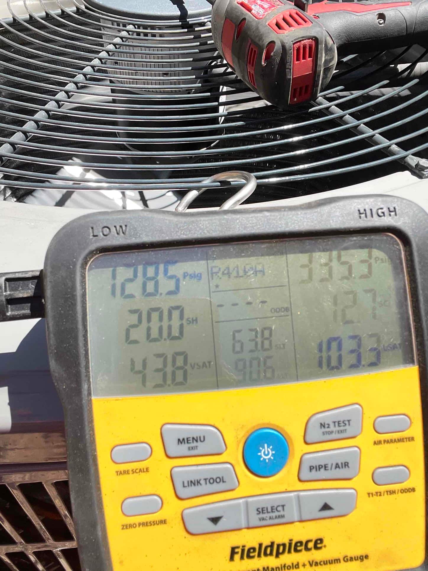 Digital manifold shows operating pressures while the outdoor condenser runs during commissioning of the new heat pump system.