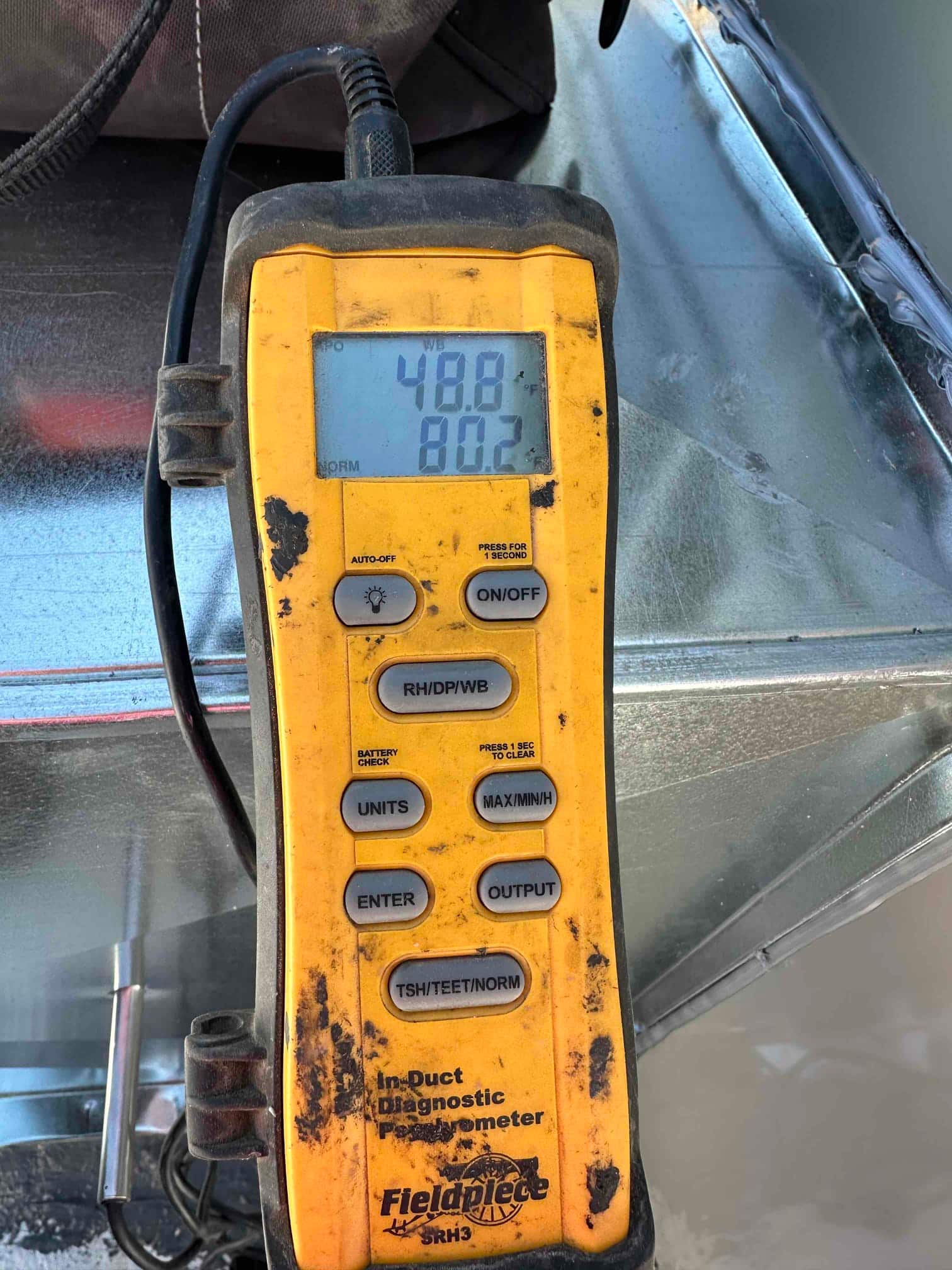 Digital probe thermometer shows 48.8°F on the upper display while checking air temperature at the duct.