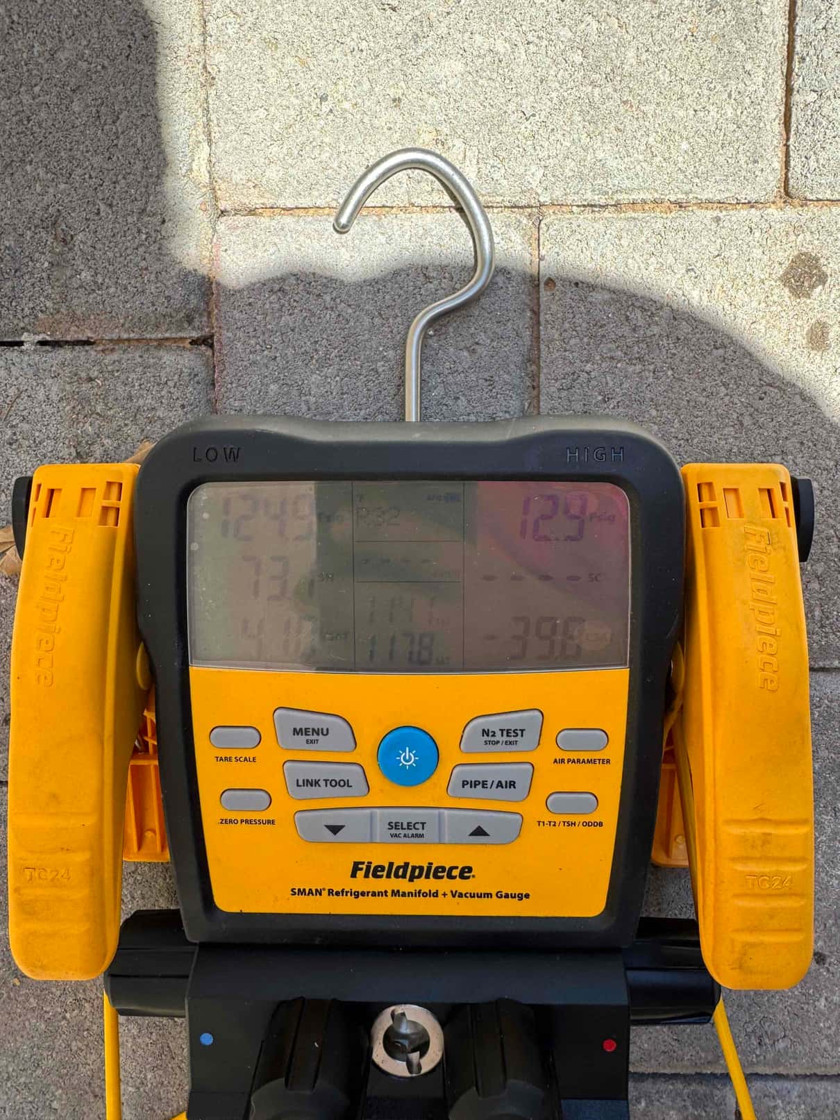 Digital refrigerant manifold with temperature clamps displayed outdoors. Screen is difficult to read due to glare, measurements not discernible.