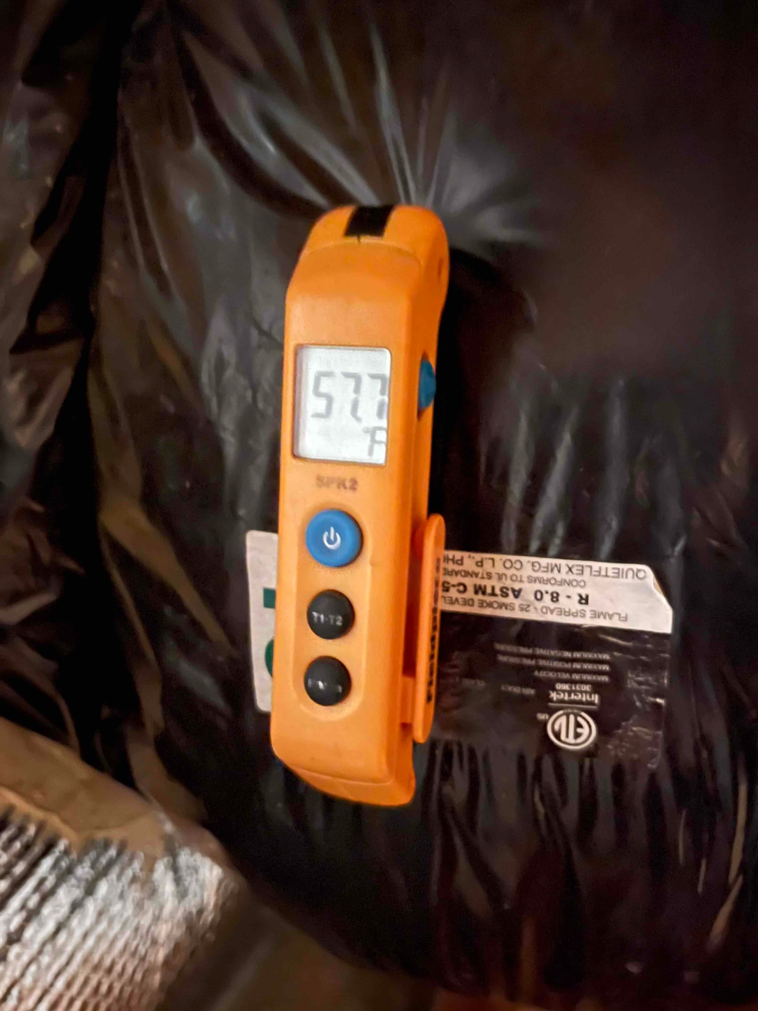 Digital thermometer clipped to insulated duct shows a surface temperature reading of 57.7 °F during diagnostic testing.