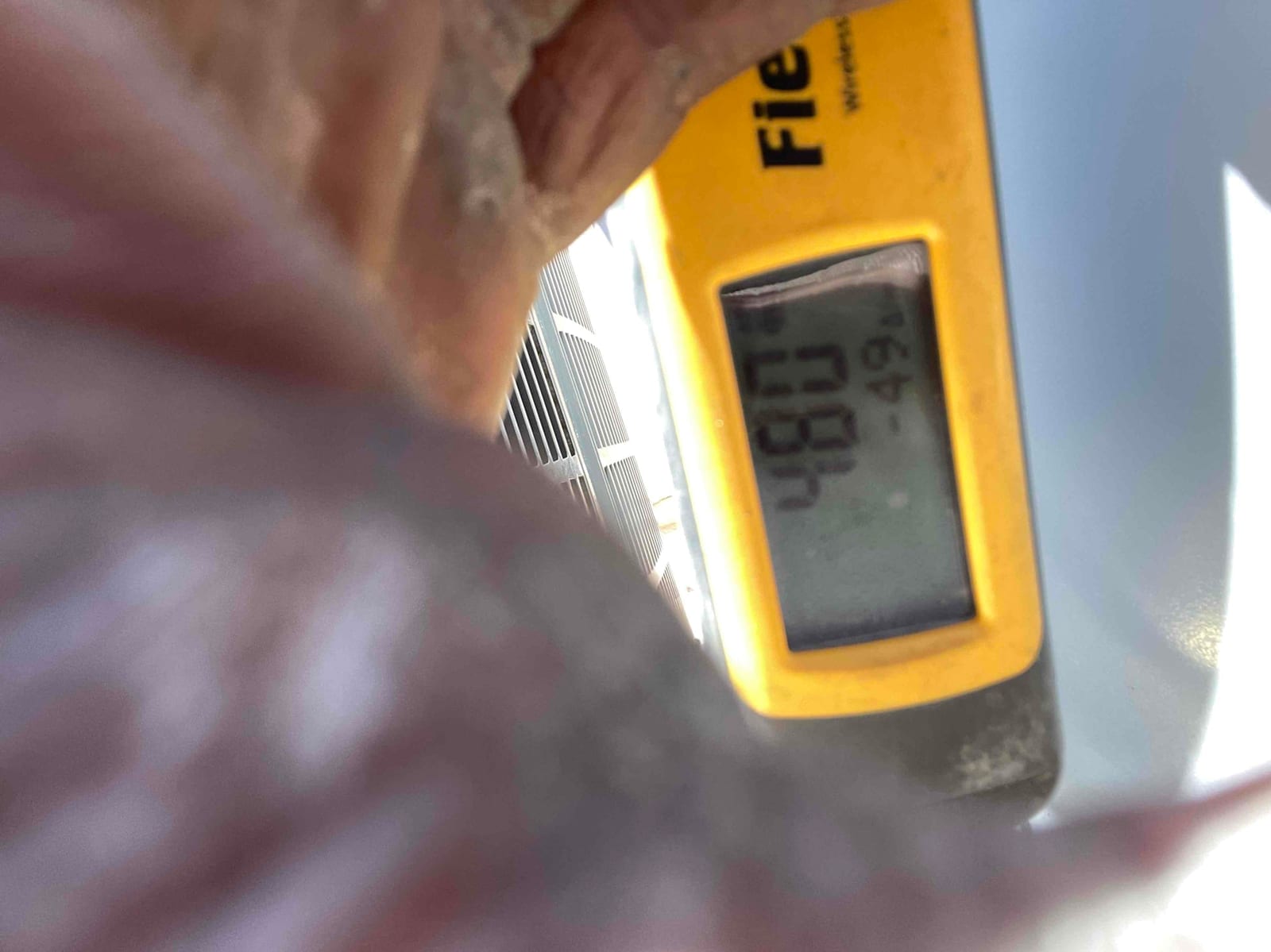 Digital thermometer display shows 48.0°F while measuring air temperature at the outdoor unit during system commissioning.