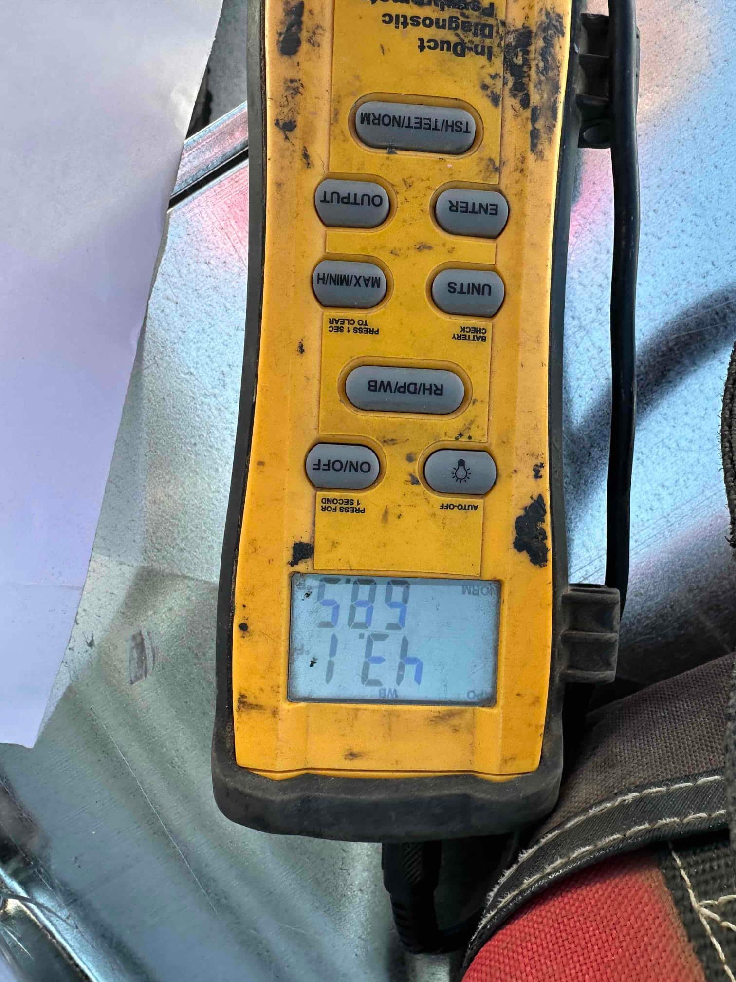Digital thermometer on ductwork displays 58.9 degrees Fahrenheit, documenting supply air temperature during commissioning.