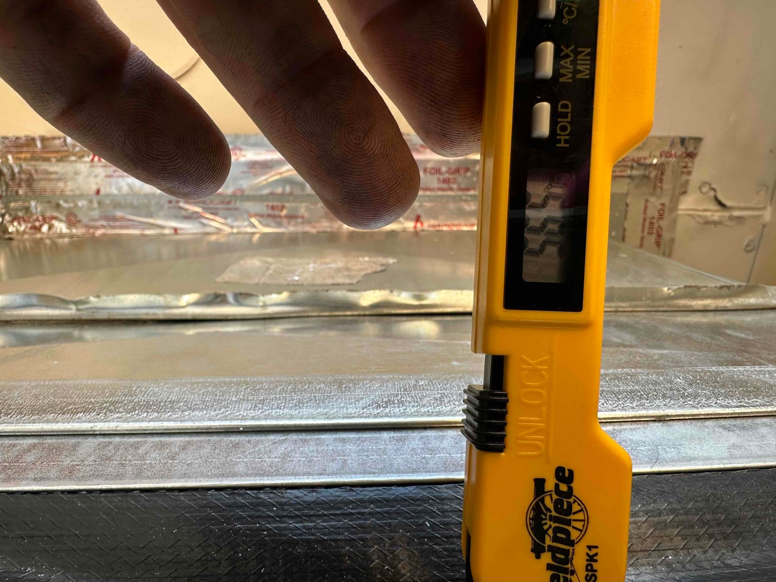Digital thermometer inserted into ductwork shows a 55°F air temperature reading during supply air check after startup.