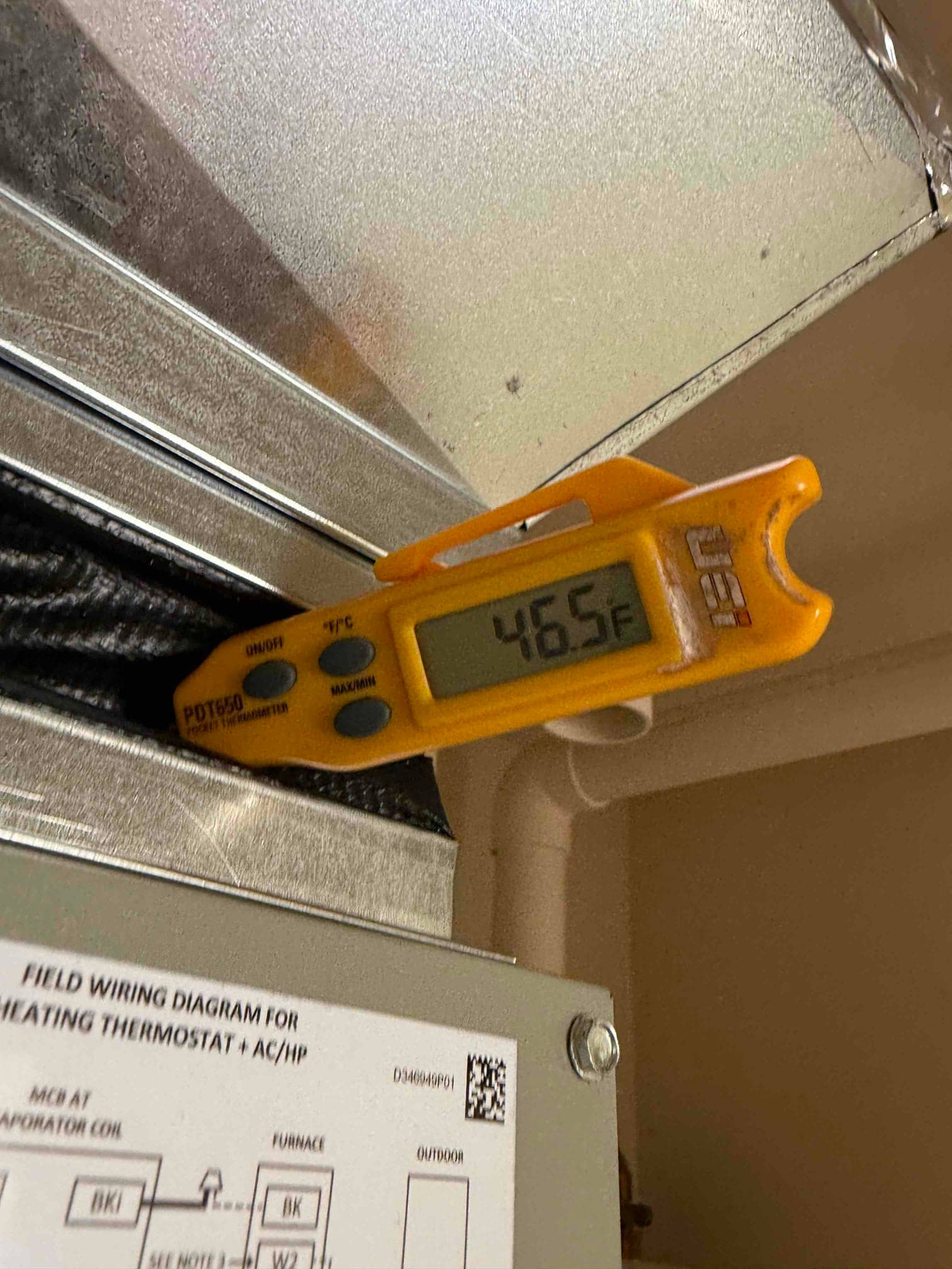 Digital thermometer inserted at the supply plenum reads 46.5°F, documenting cooled air temperature leaving the evaporator.