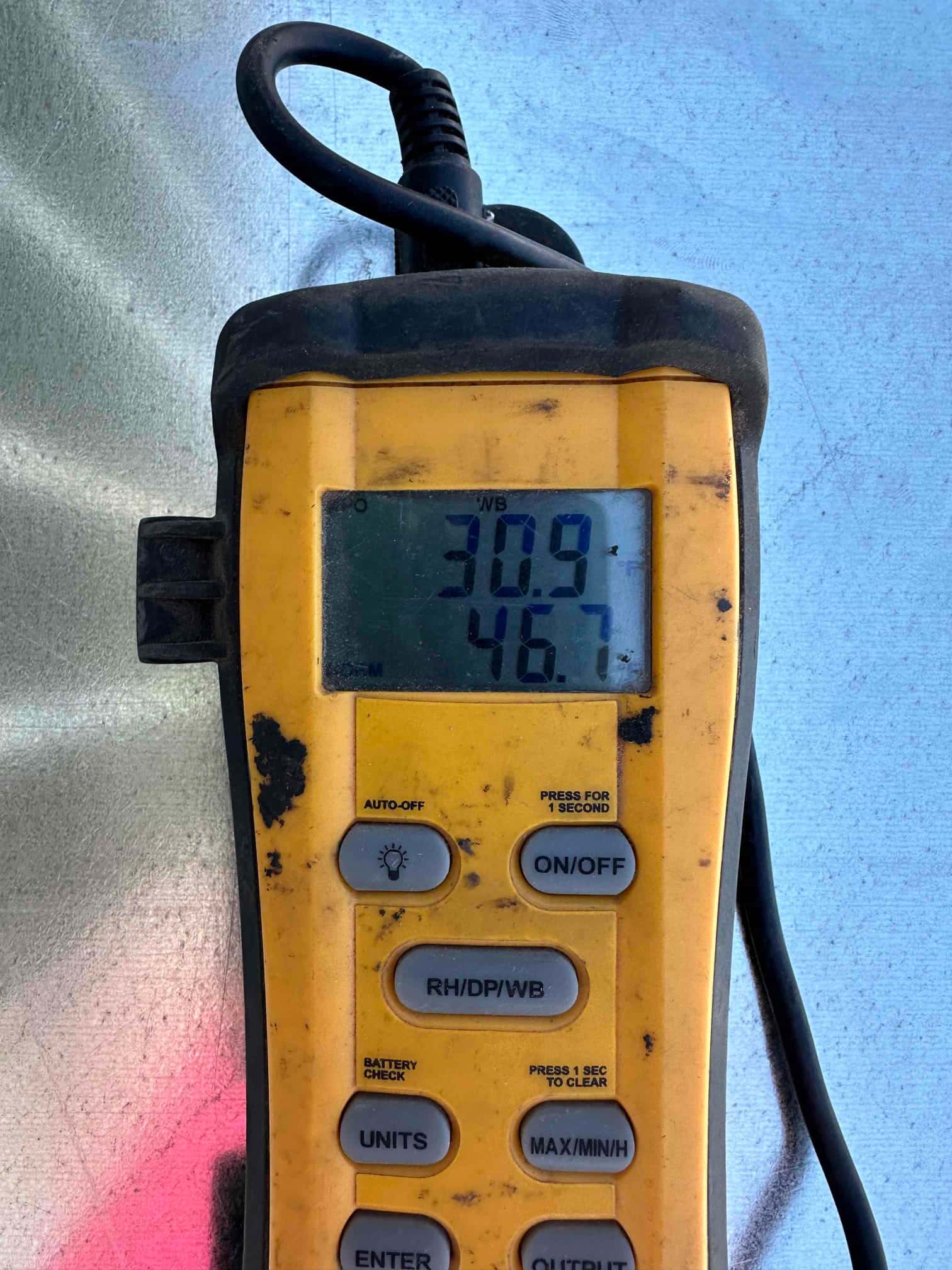 Digital thermometer shows 46.7°F, documenting cold supply air temperature during commissioning of the cooling system.