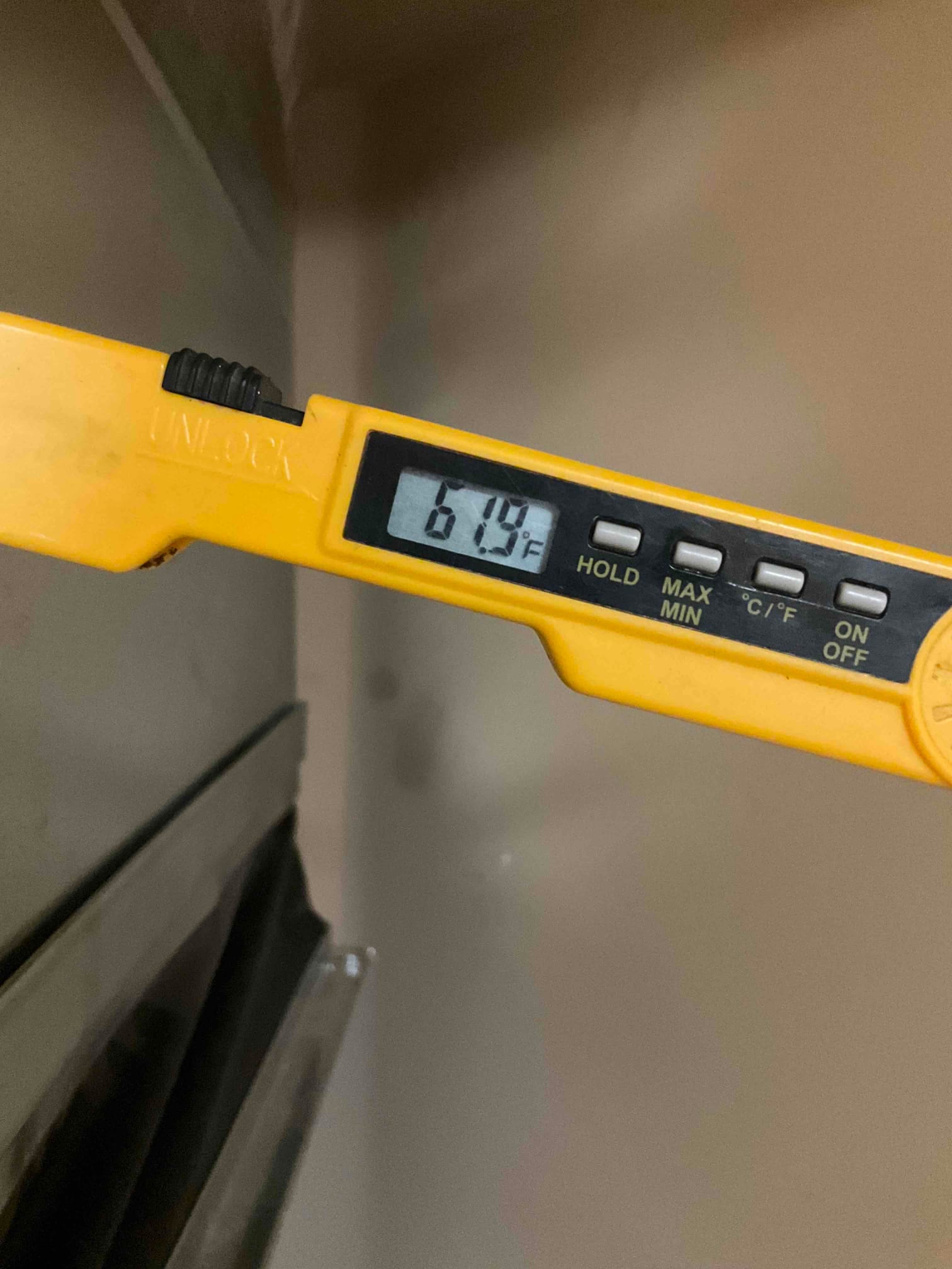 Digital thermometer shows 61.9°F while measuring air temperature at the HVAC system outlet.