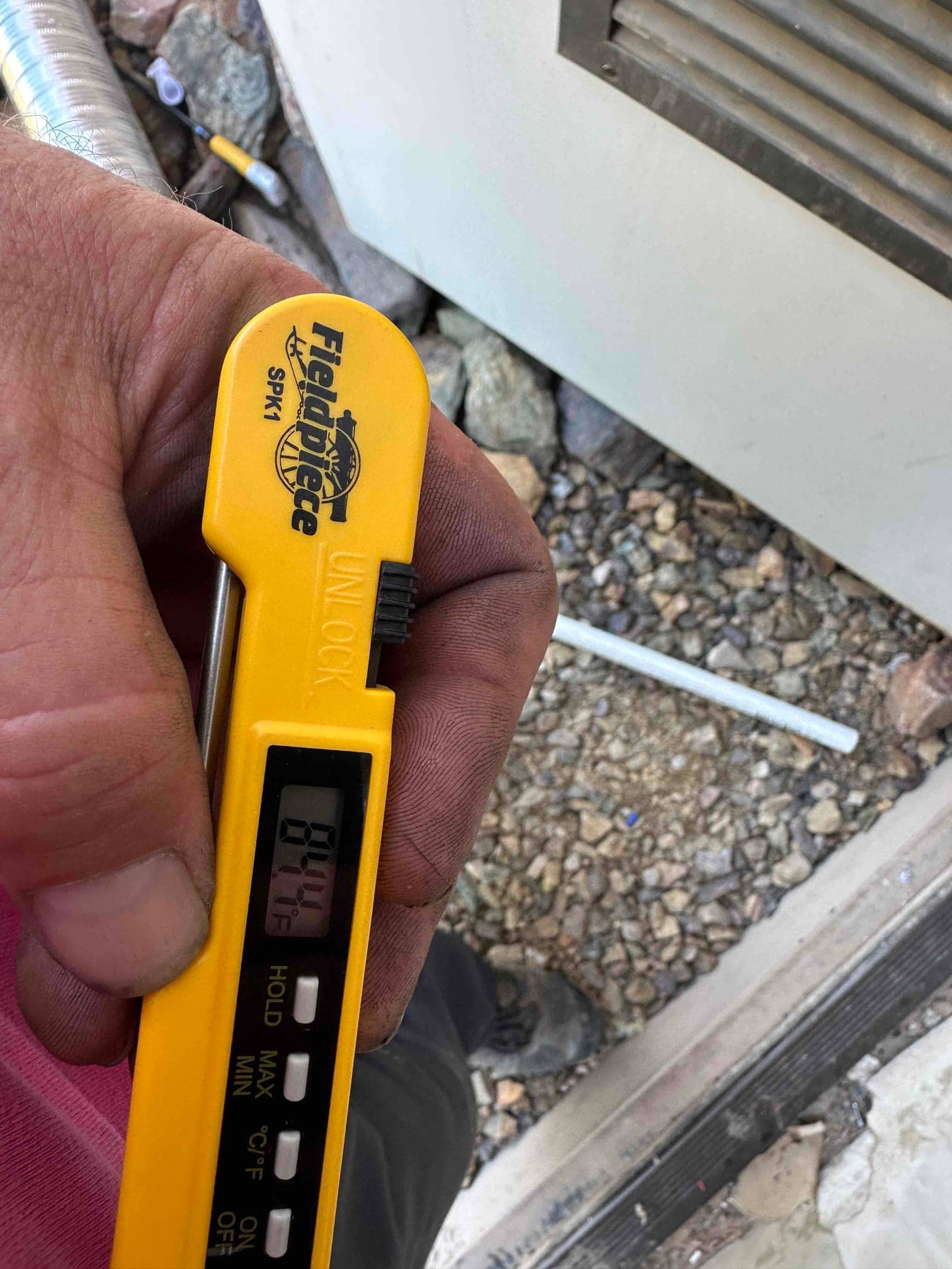 Digital thermometer shows 84.1°F while checking air temperature during system commissioning at the outdoor unit area.