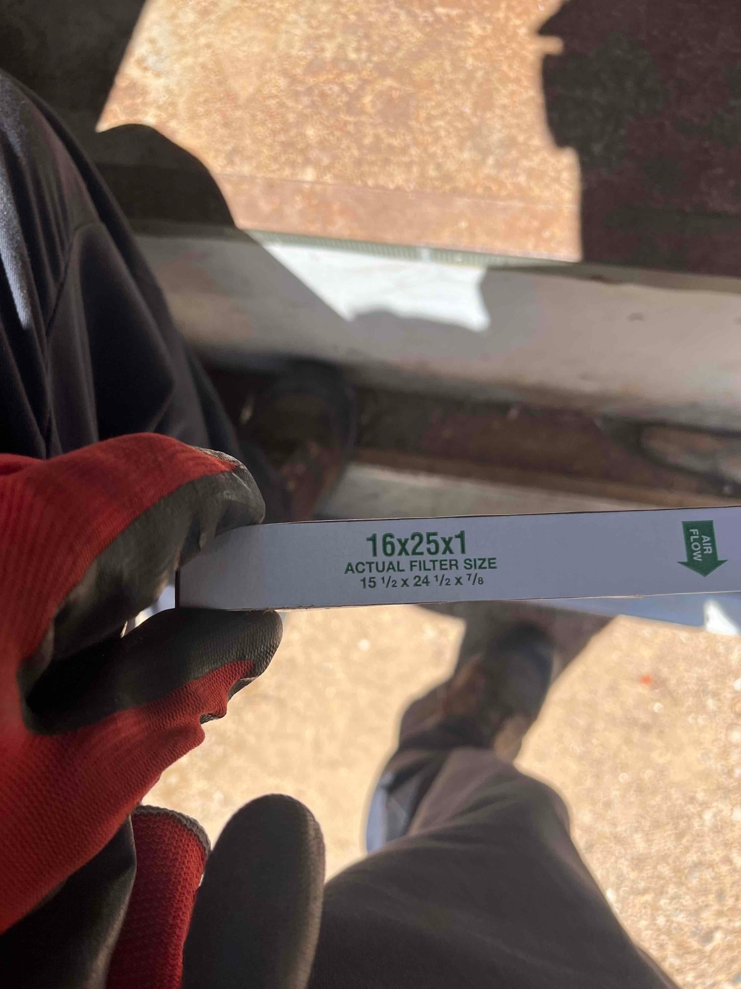 Disposable HVAC air filter labeled 16x25x1 with airflow arrow, held by a gloved technician during installation.