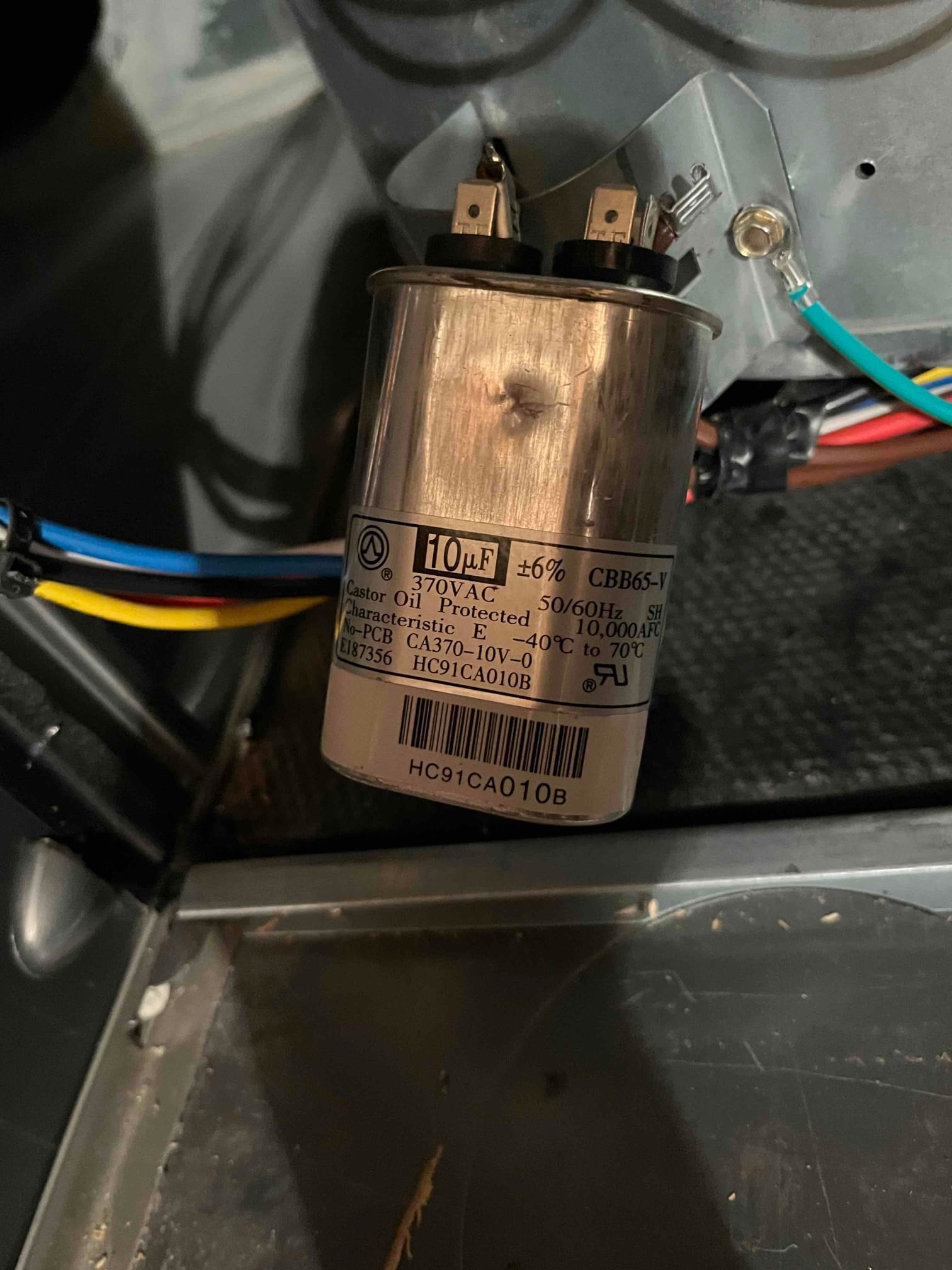 Dual-run capacitor inside the air handler compartment, labeled 10 μF ±6%, 370 VAC, with connected spade terminals and attached wiring.