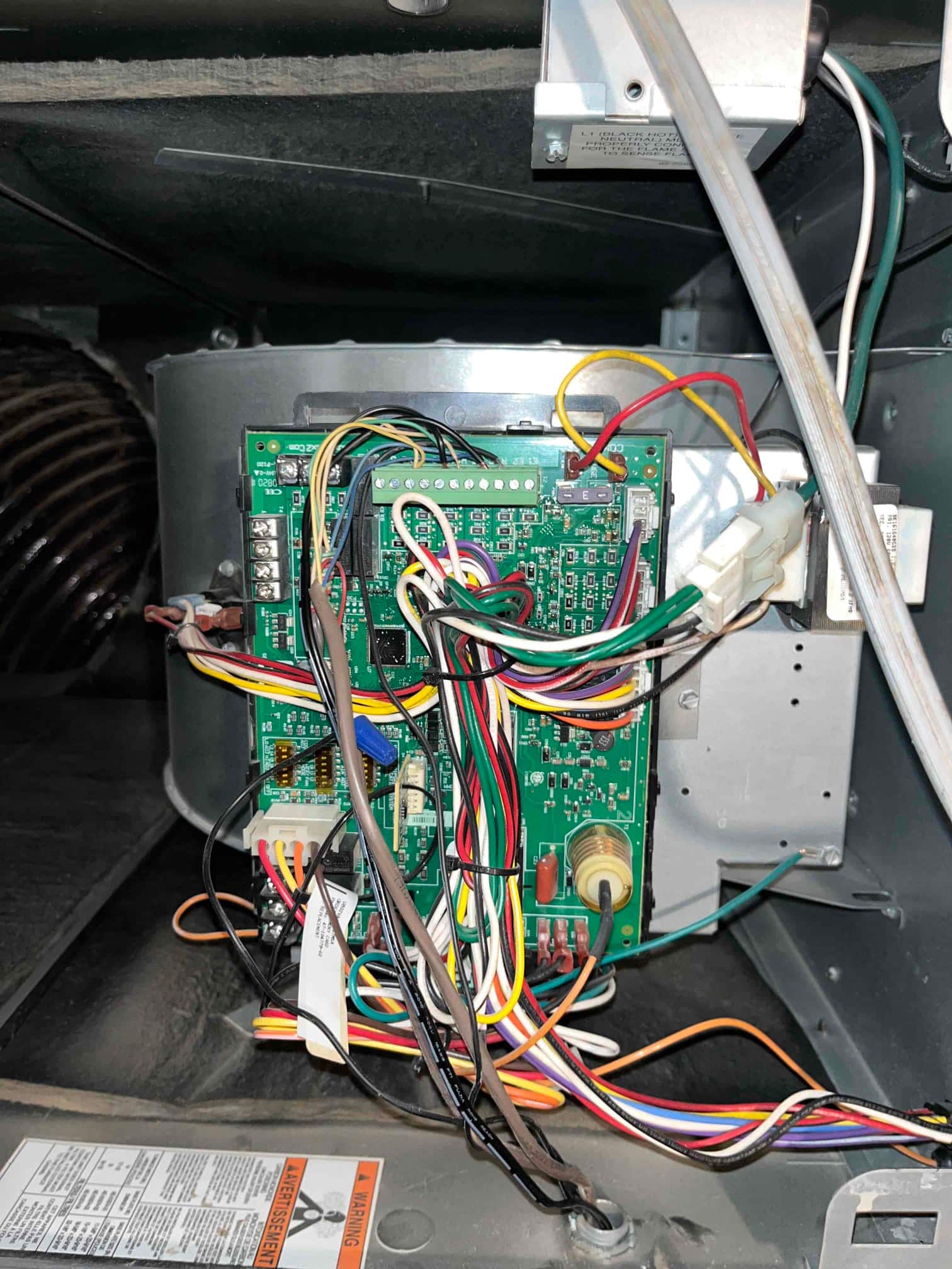 Furnace control board with multiple connected wires inside the air handler cabinet, showing harnesses, terminals, and mounting hardware.