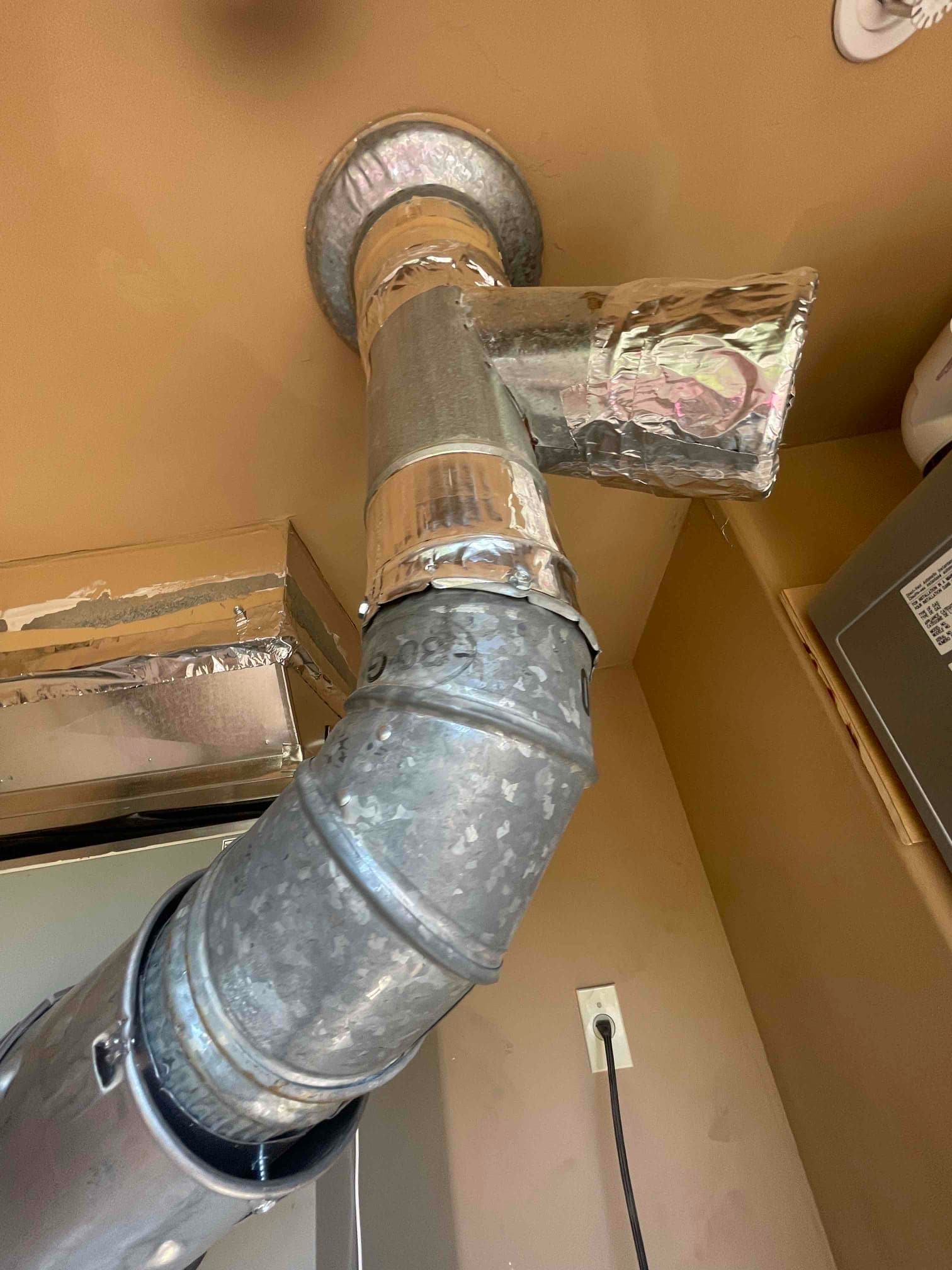 Galvanized vent piping with sealed joints and a capped wye fitting near the ceiling beside the indoor unit.