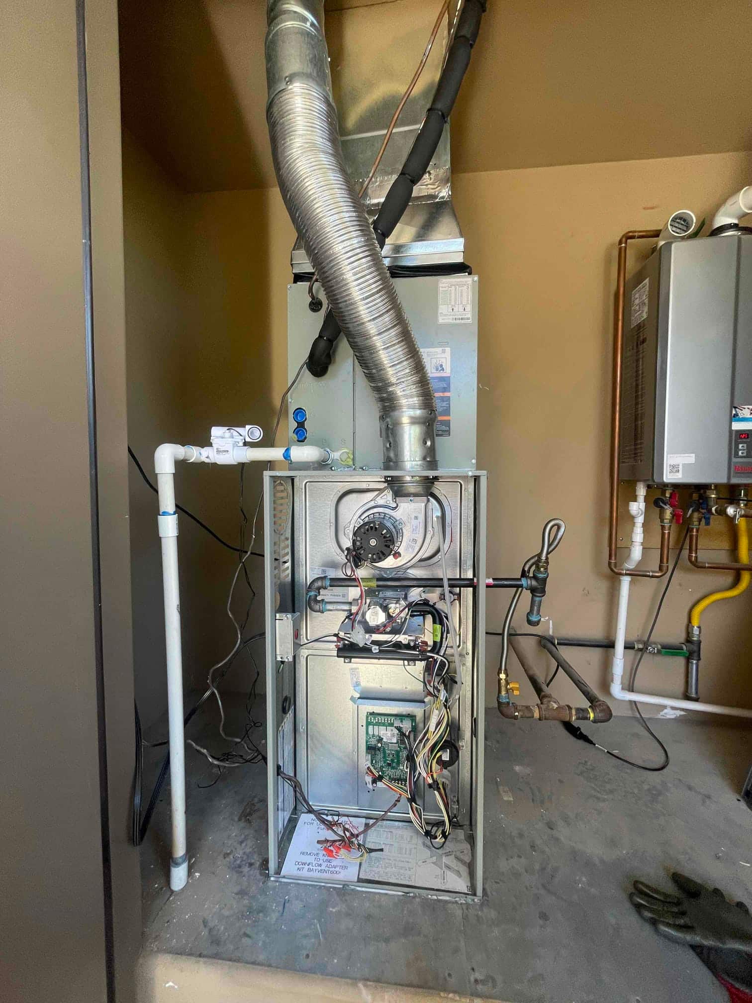 Gas furnace and evaporator coil installed with venting, condensate drain, insulated refrigerant lines, and open blower compartment during commissioning.