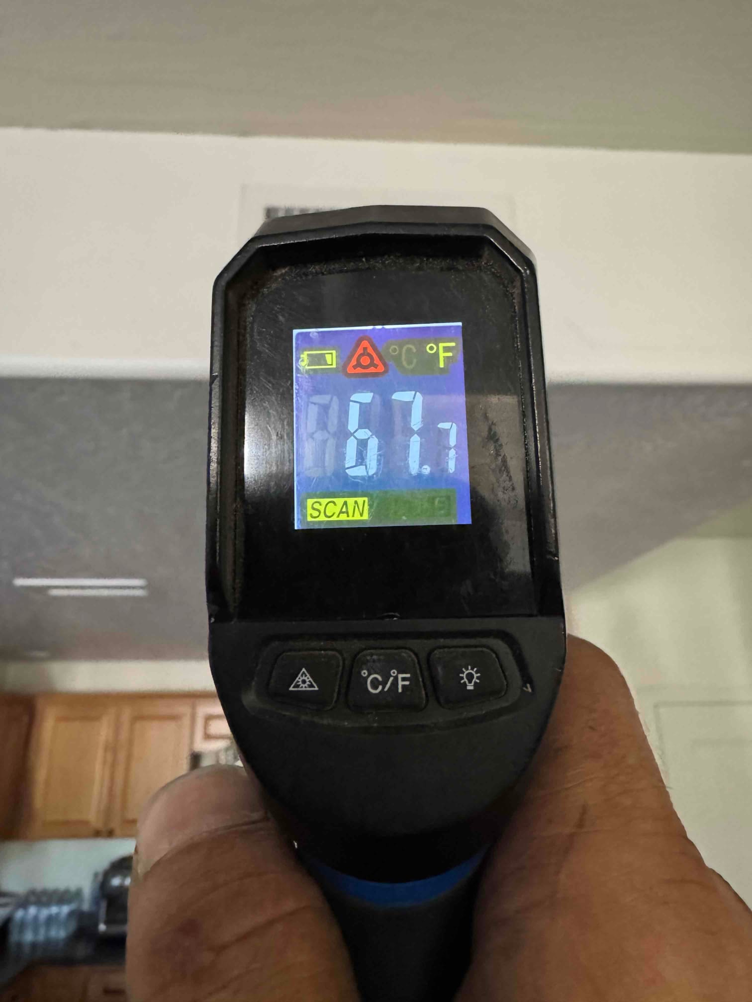 Handheld infrared thermometer displays 67.7 degrees Fahrenheit while scanning indoor air during commissioning checks.