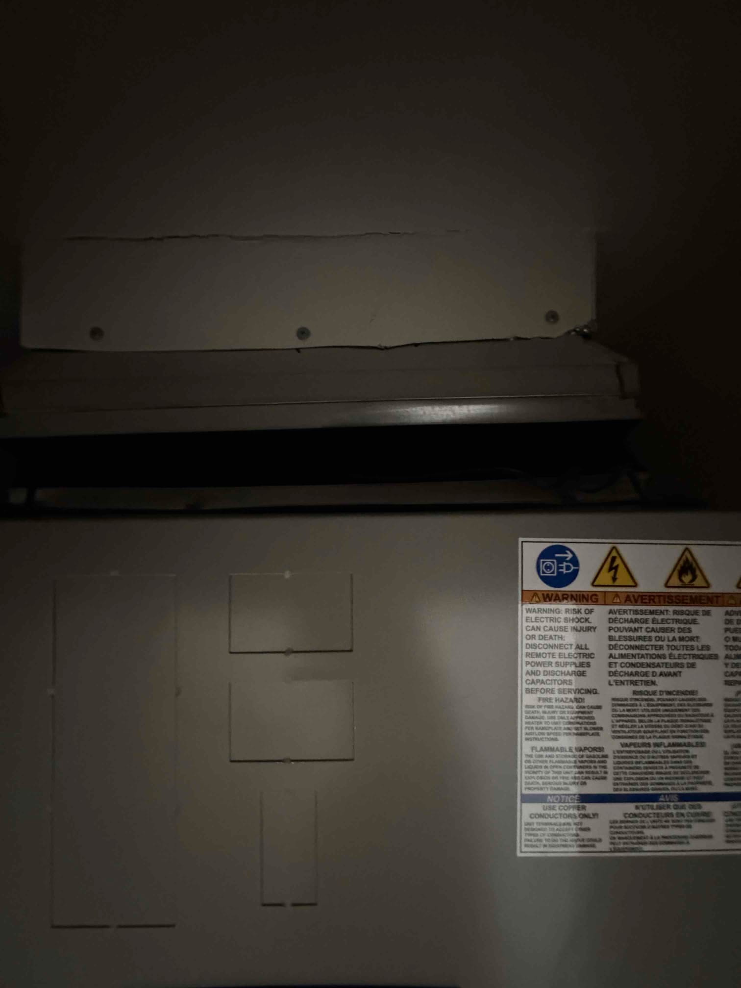 Indoor air handler cabinet with sealed sheet metal cover and safety warning label visible in a utility space.