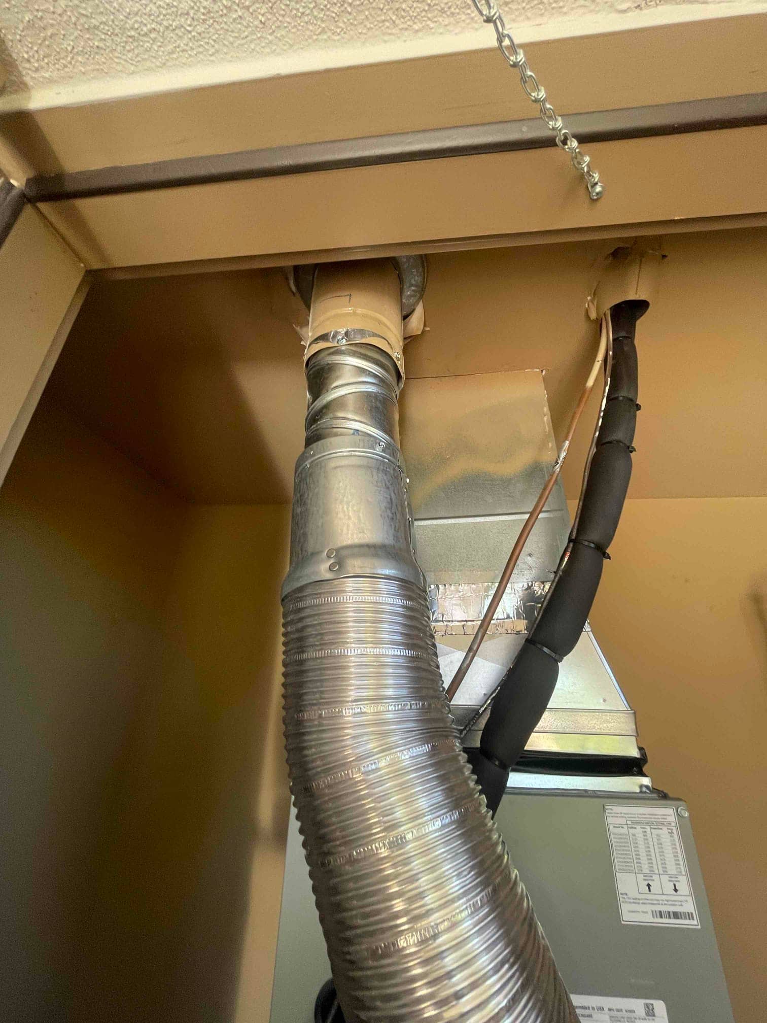 Indoor air handler with insulated refrigerant lines and metal vent ducting routed through the cabinet opening after installation.