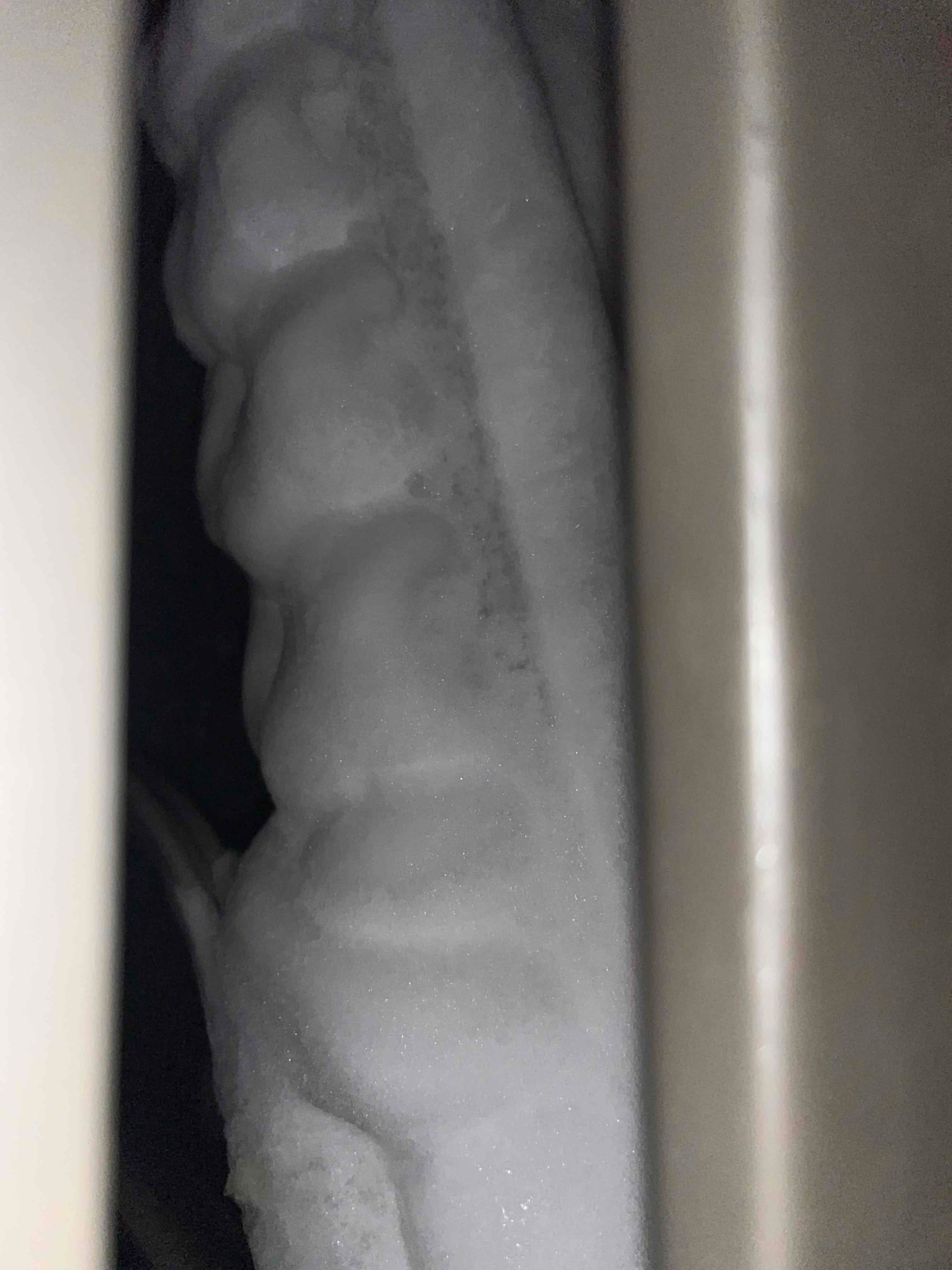 Indoor evaporator coil heavily iced over, showing thick frost accumulation along the coil surface and tubing.