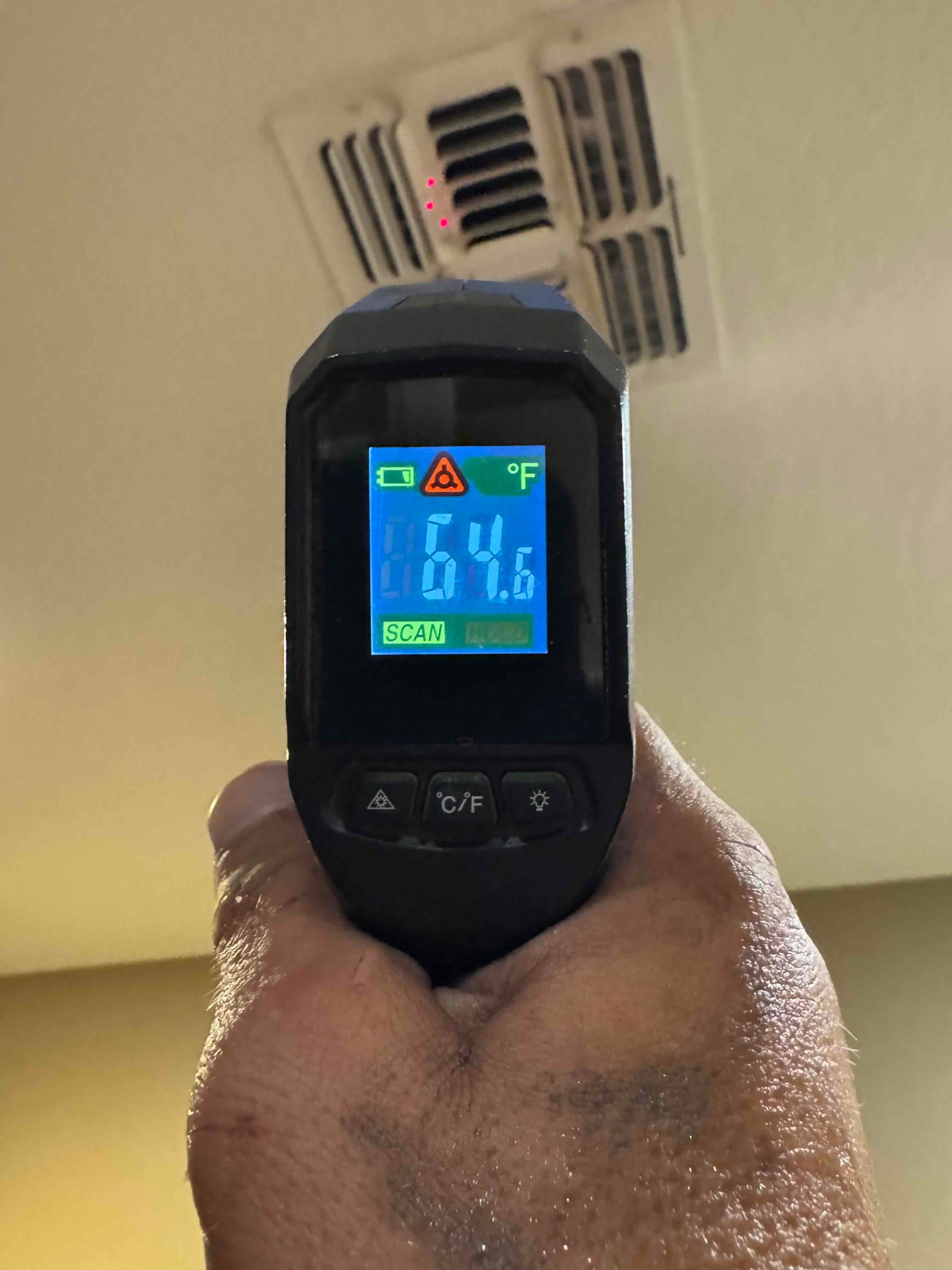 Infrared thermometer aimed at a ceiling supply register shows 64.6°F during cooling performance check.
