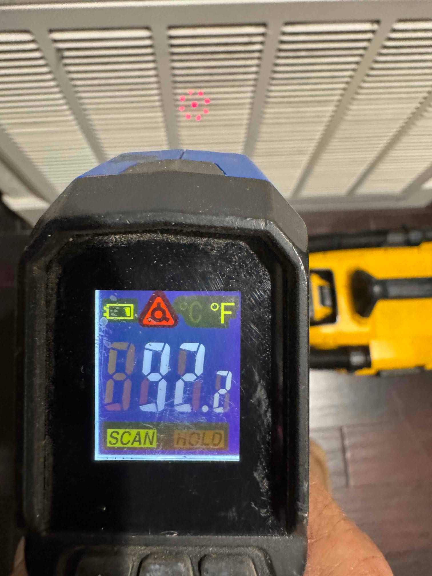 Infrared thermometer aimed at a return grille displays temperature in degrees Fahrenheit during airflow checks.
