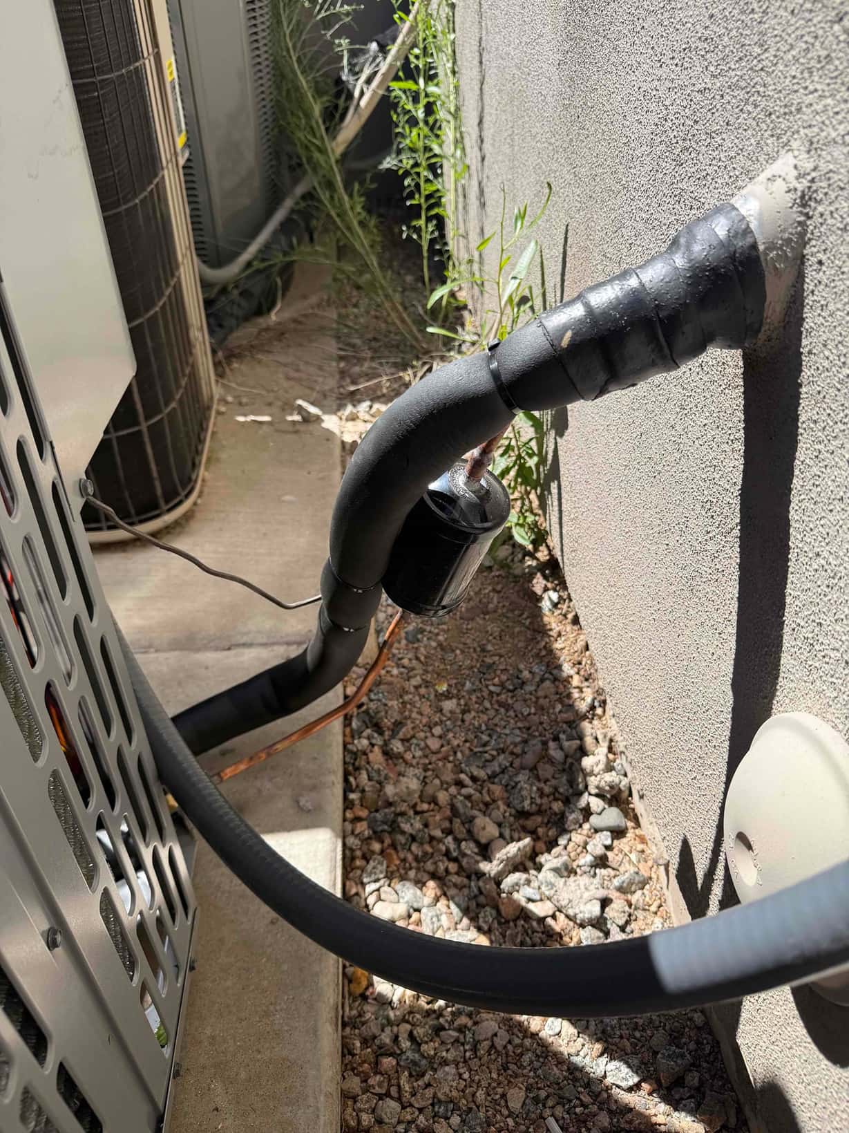 Insulated refrigerant lines with a suction line filter-drier exit the wall and connect to the new outdoor condenser.