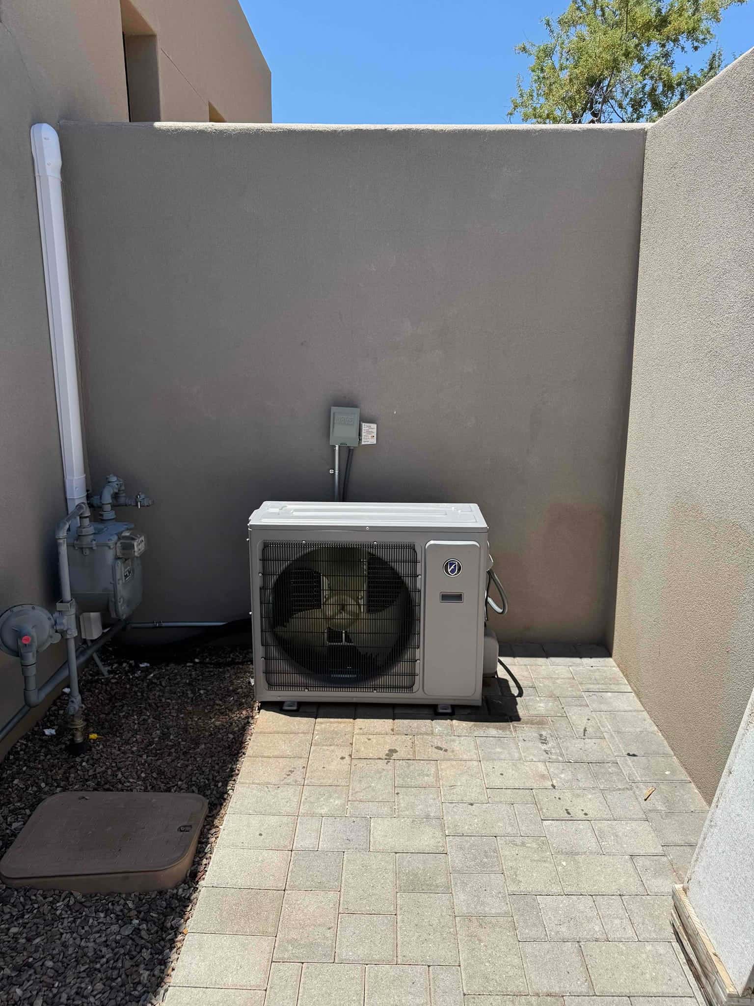 Mini-split outdoor unit set on a level paver pad with disconnect and line-set cover mounted on the wall.