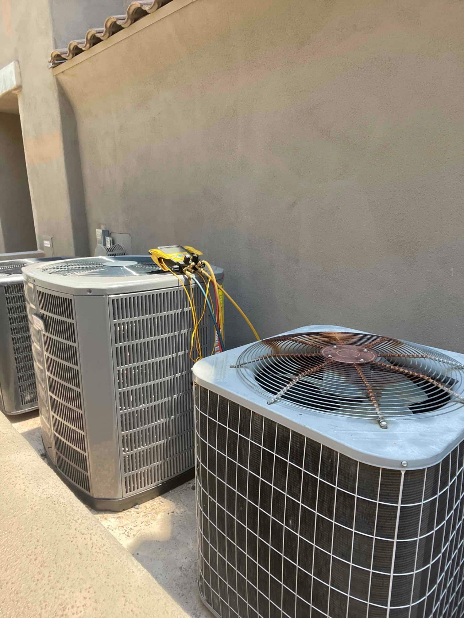 Multiple outdoor condensers installed on a concrete pad, with manifold gauge set connected to the middle unit for commissioning.