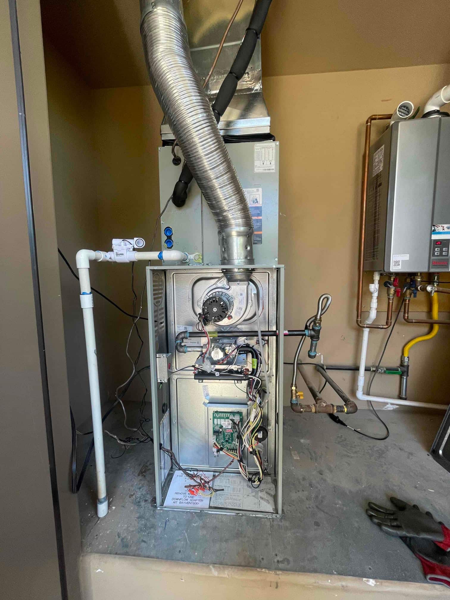 New air handler and furnace installed with connected ducting, condensate drain, insulated refrigerant lines, and control wiring visible during setup.