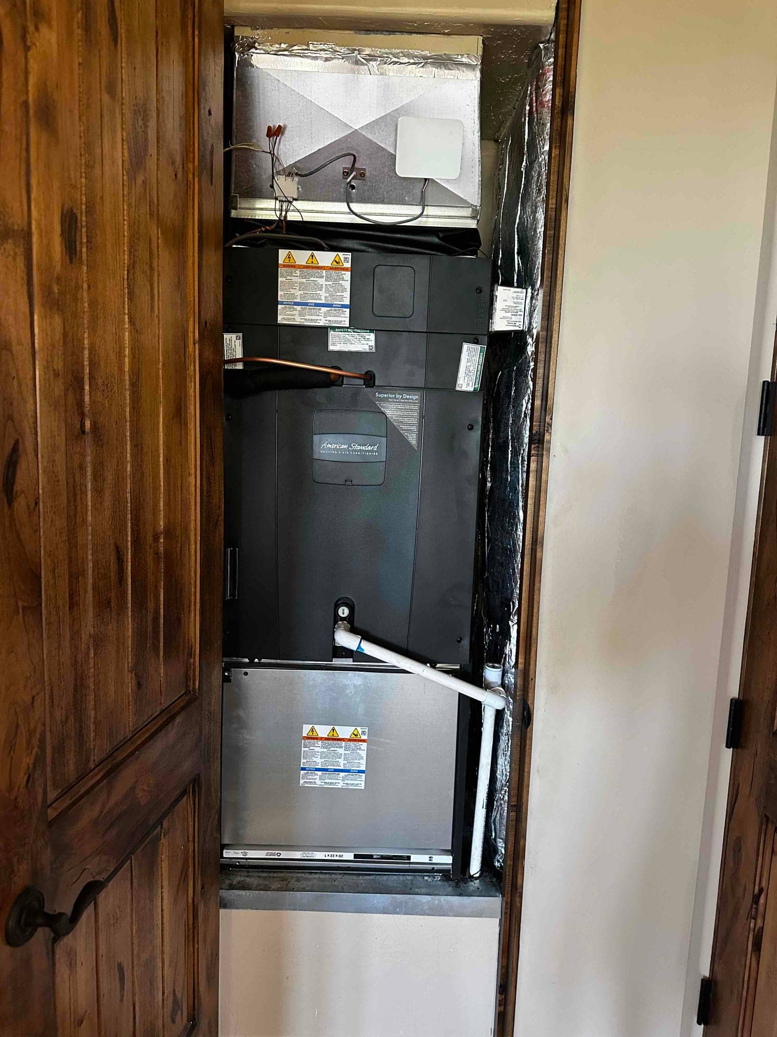 New air handler installed in a closet, with insulated duct connection and PVC condensate drain piping routed to the side.