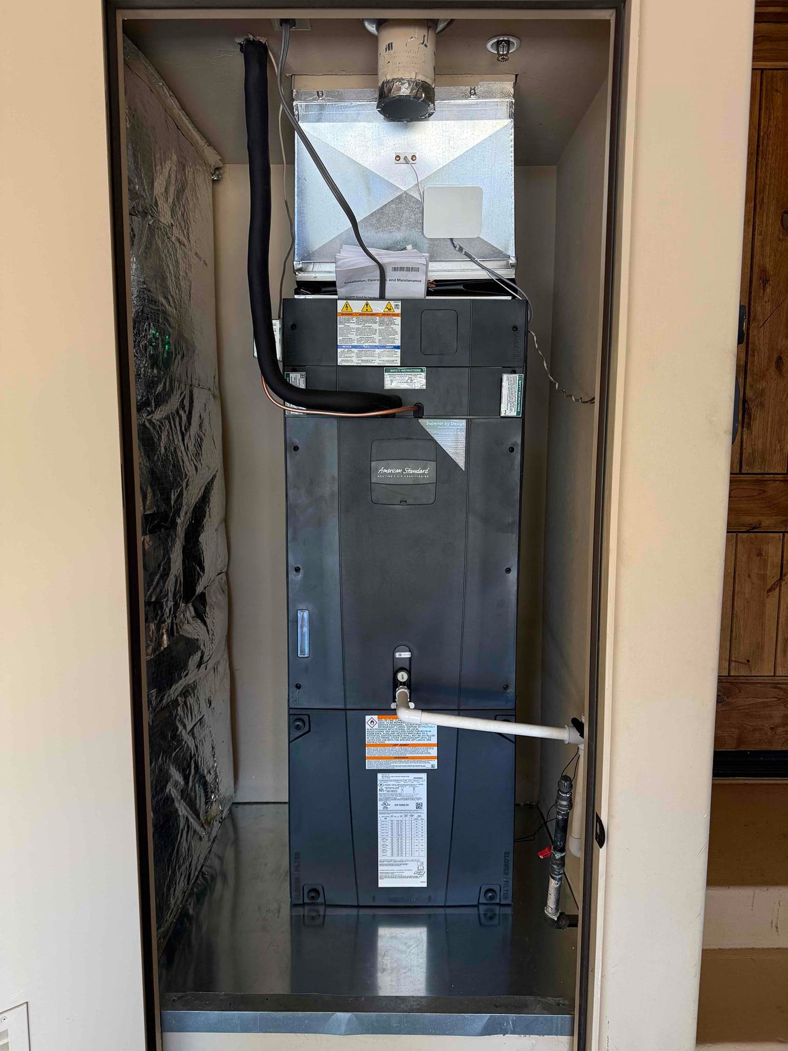 New air handler installed in closet with insulated refrigerant line, metal drain pan, condensate trap, and sealed supply plenum.