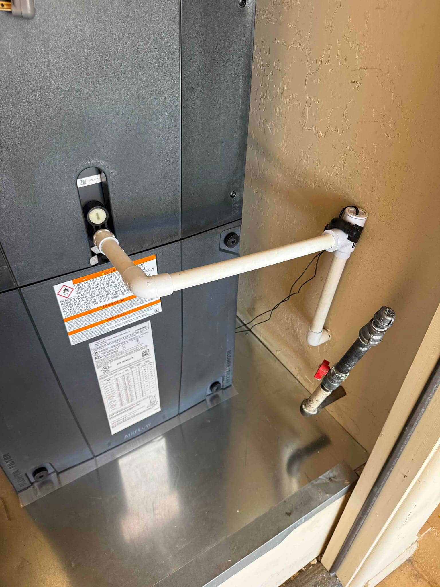 New air handler set on a metal drain pan with installed PVC condensate drain and external cleanout tee.