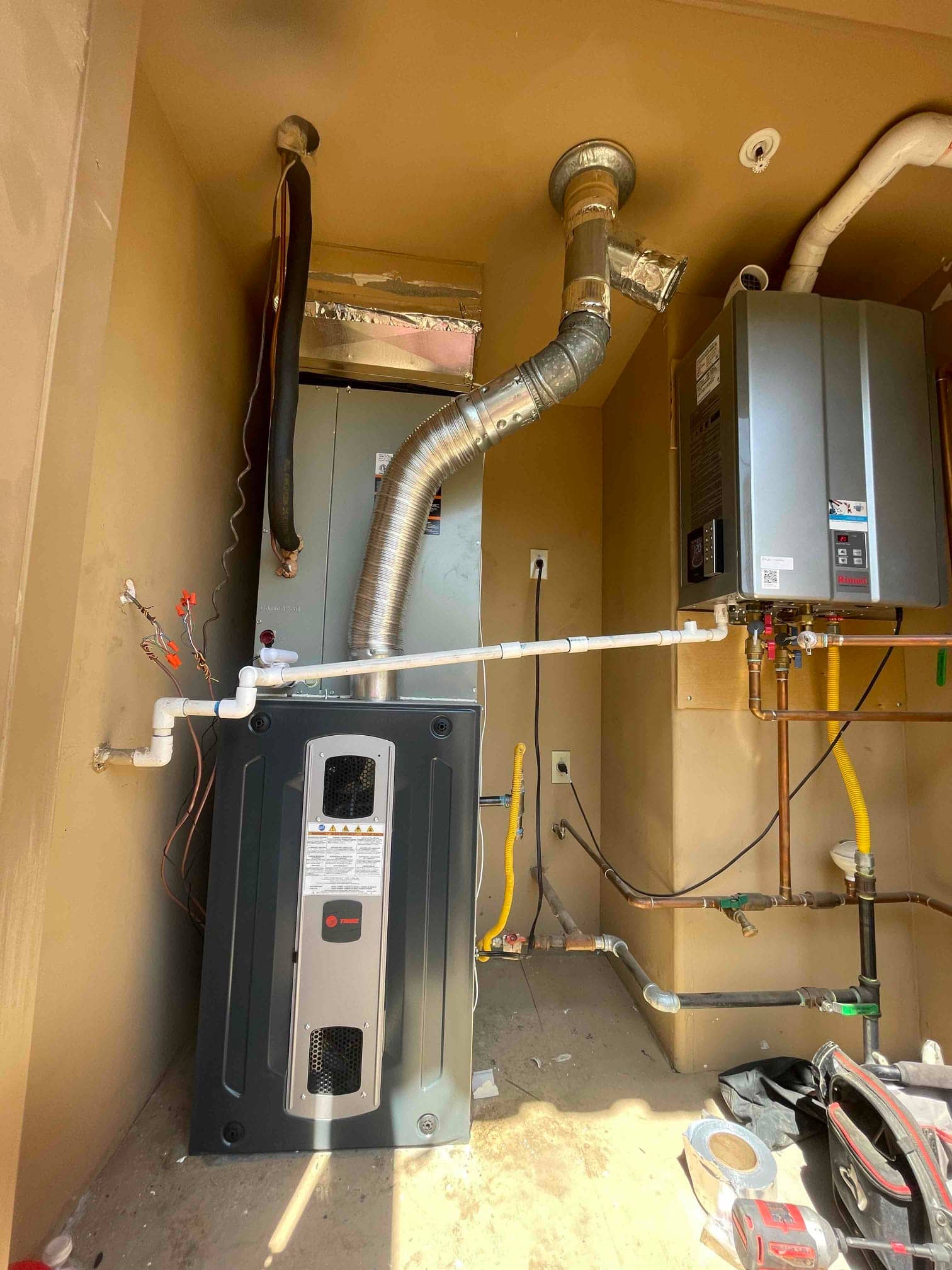 New furnace and air handler installed with venting, condensate drain, gas piping, and duct connections in a utility room.
