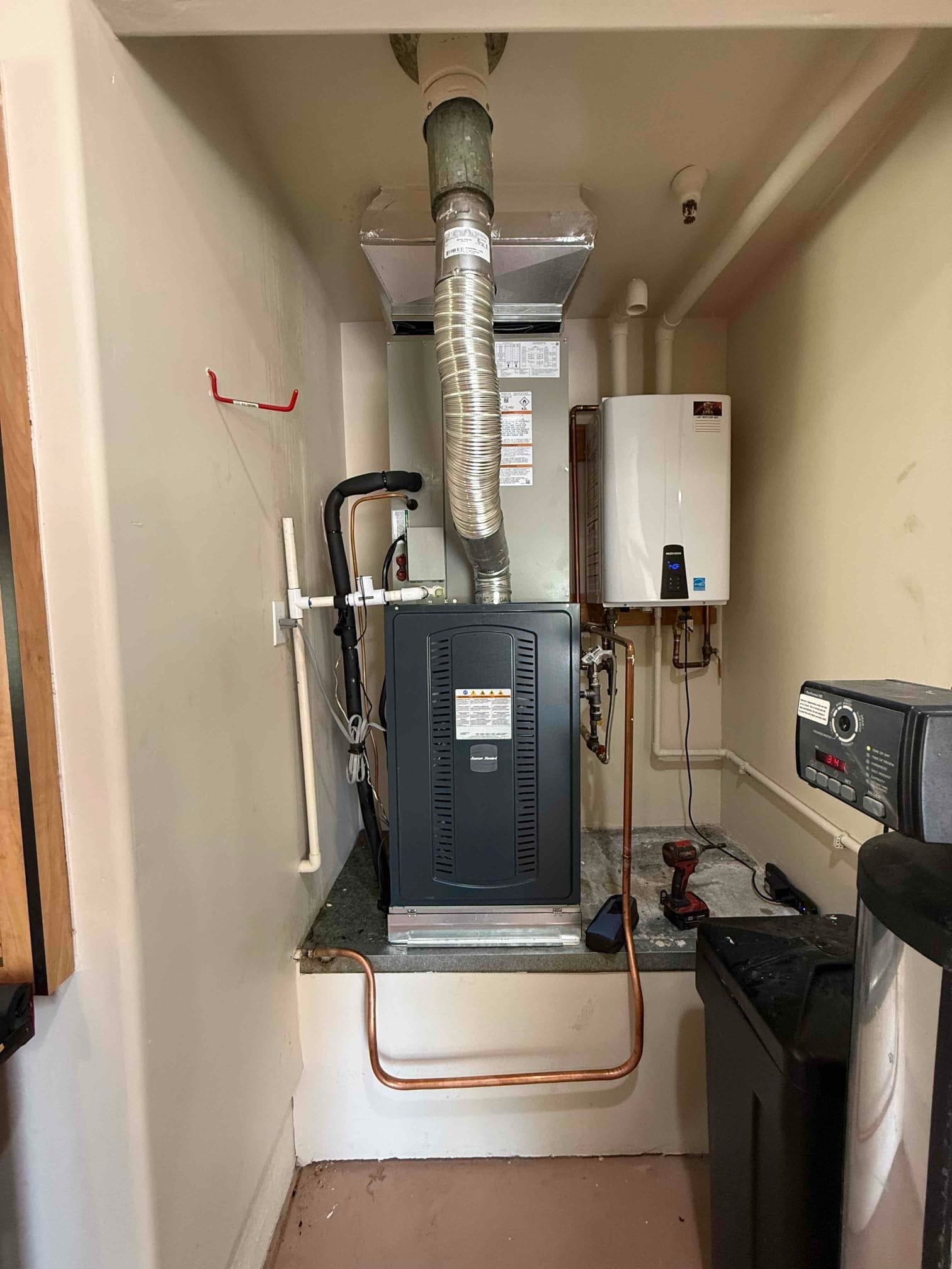 New furnace and coil installed on a platform with venting, insulated refrigerant lines, condensate piping, and adjacent tankless water heater.