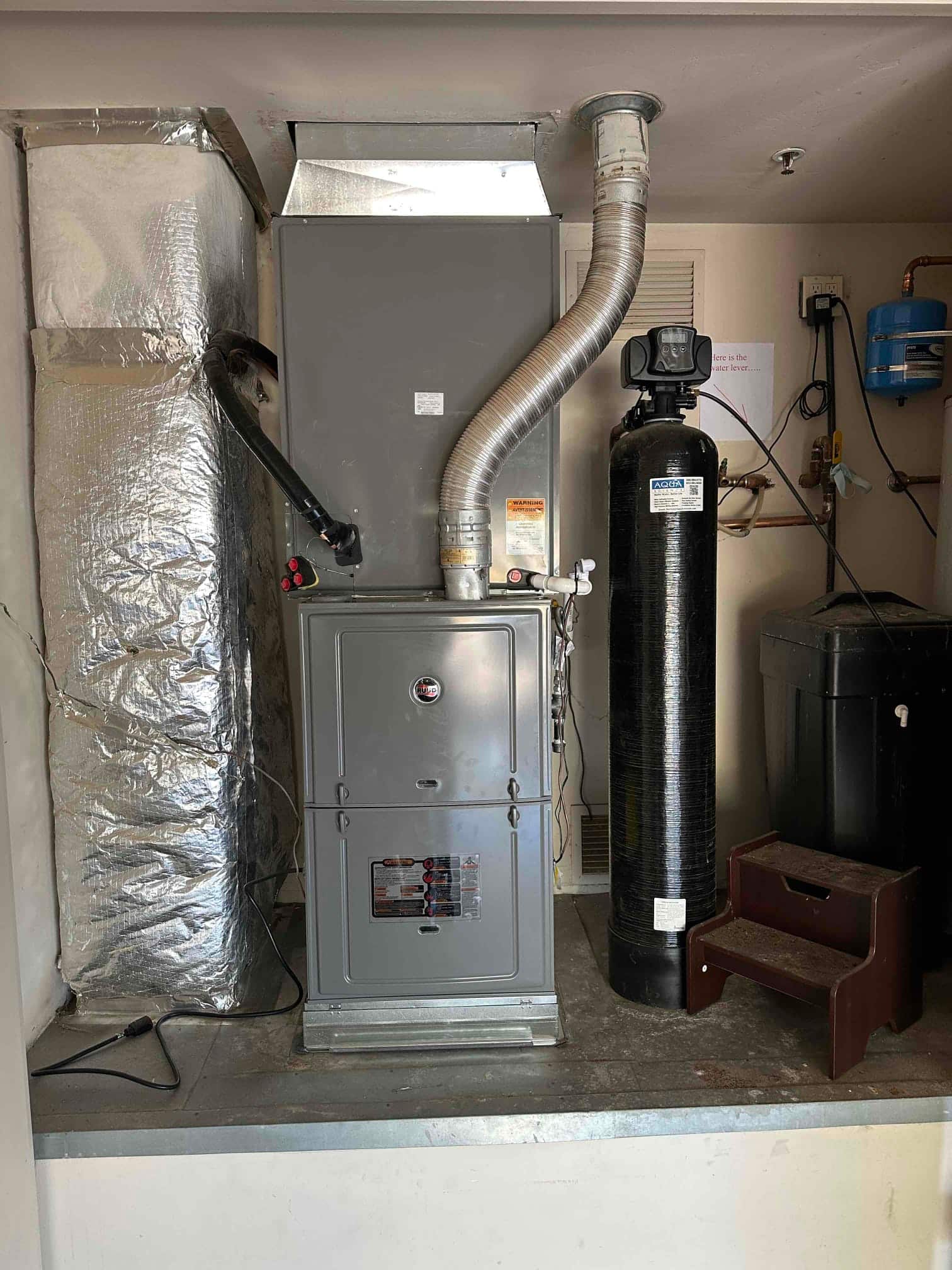 New furnace and evaporator air handler installed with insulated duct connections and venting, set on a raised platform in the utility area.
