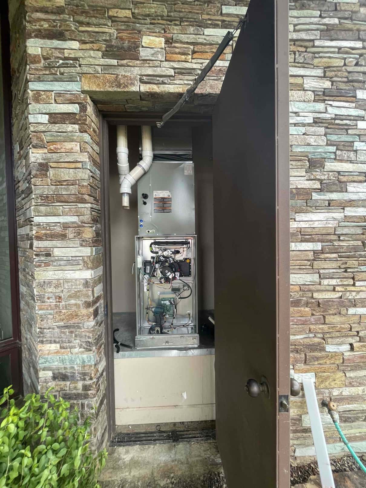 New furnace installed in exterior closet with PVC intake and exhaust venting; front panel open showing burner and control wiring.