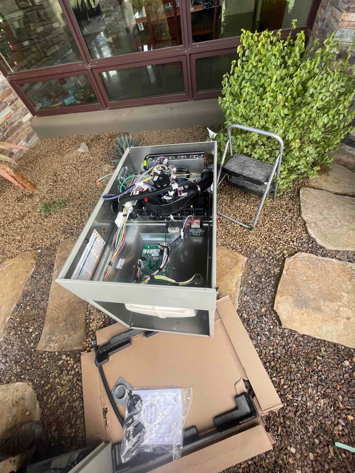 New gas furnace cabinet opened outdoors during staging, showing control board, wiring harnesses, inducer assembly, and included hardware on packaging.