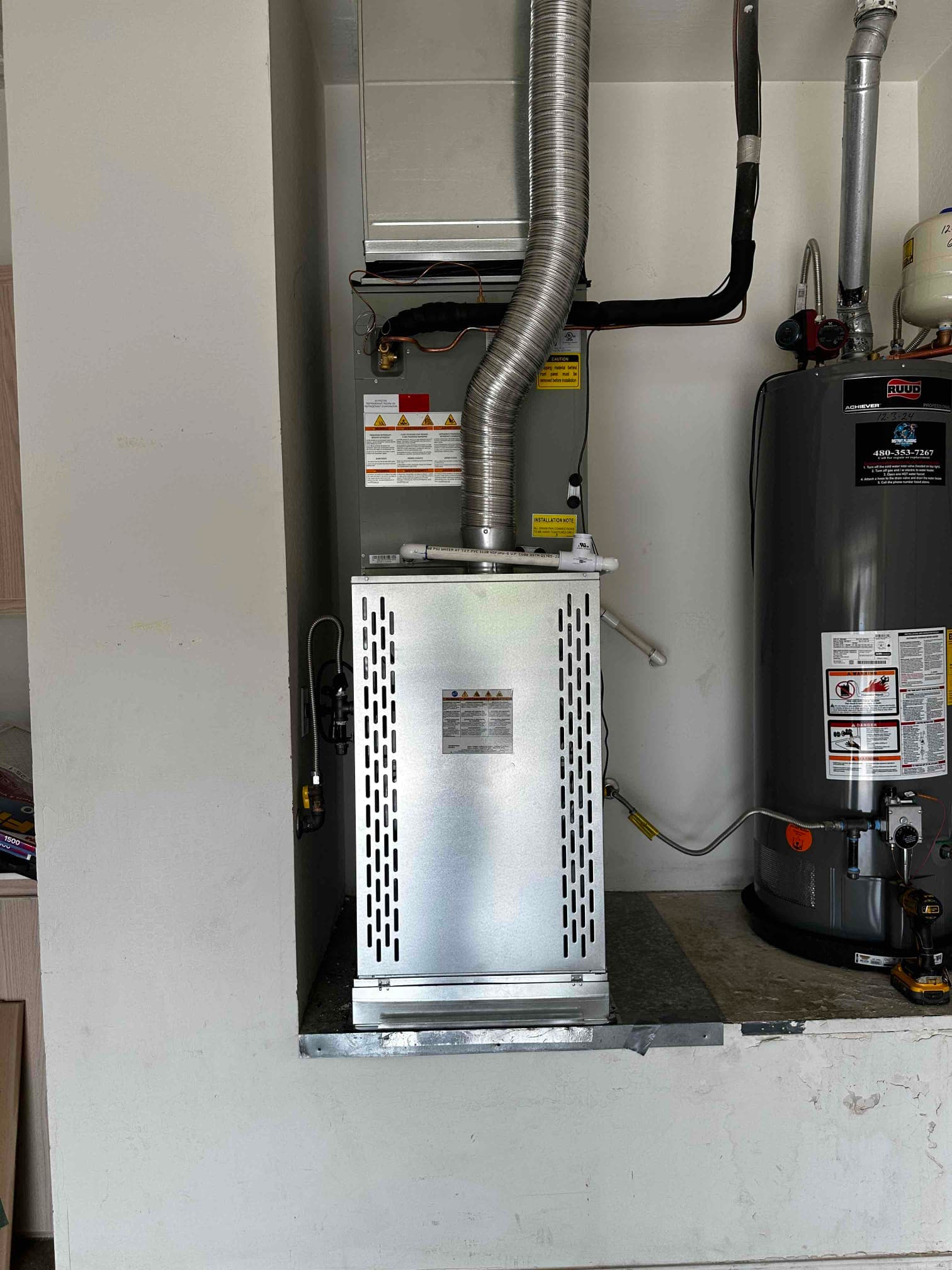 New gas furnace and evaporator coil installed with flue vent, insulated refrigerant lines, condensate drain, and adjacent water heater in garage alcove.