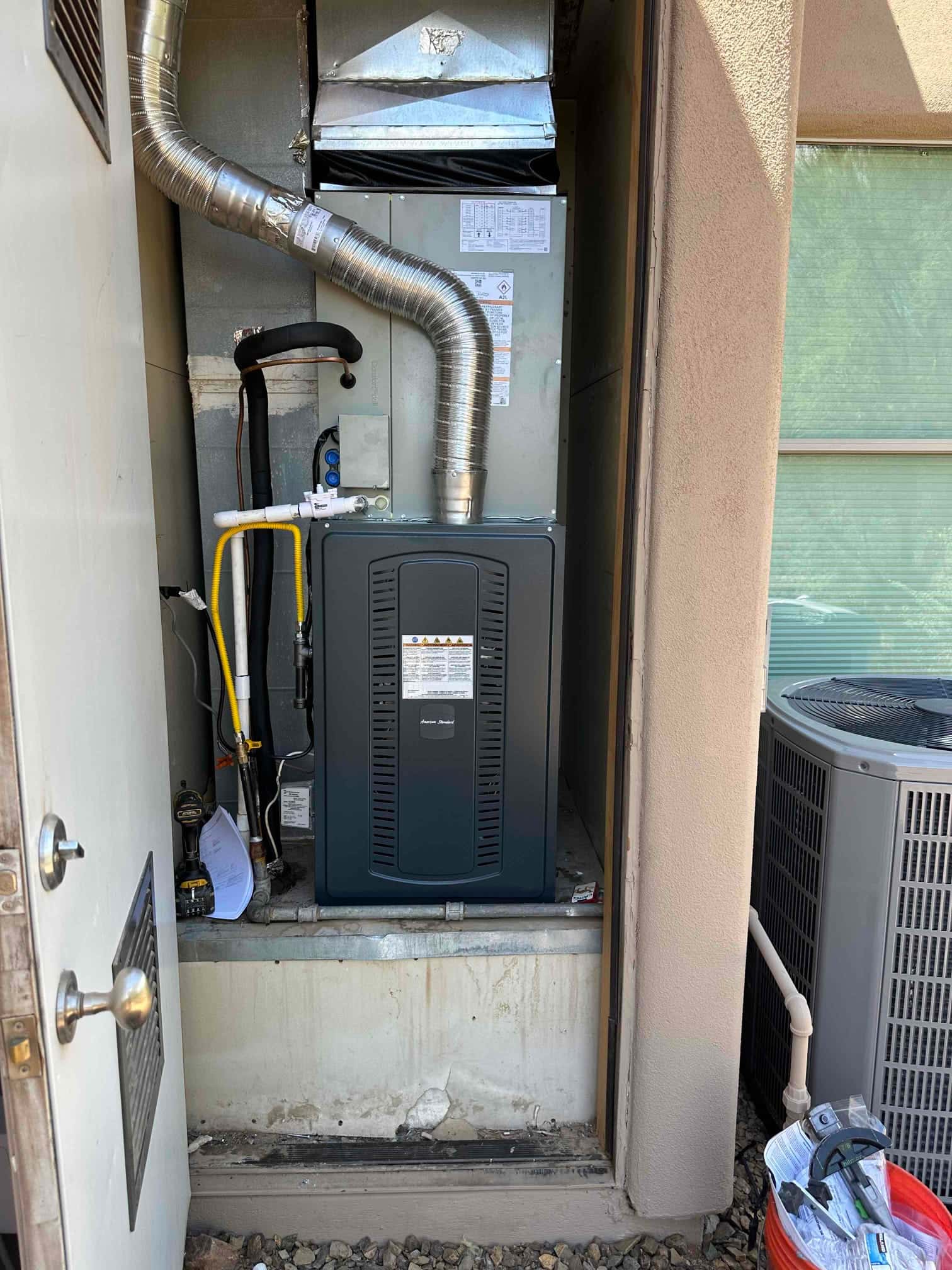 New gas furnace and evaporator installed in an exterior closet with venting, drain, and insulated refrigerant lines; matching outdoor condenser adjacent.