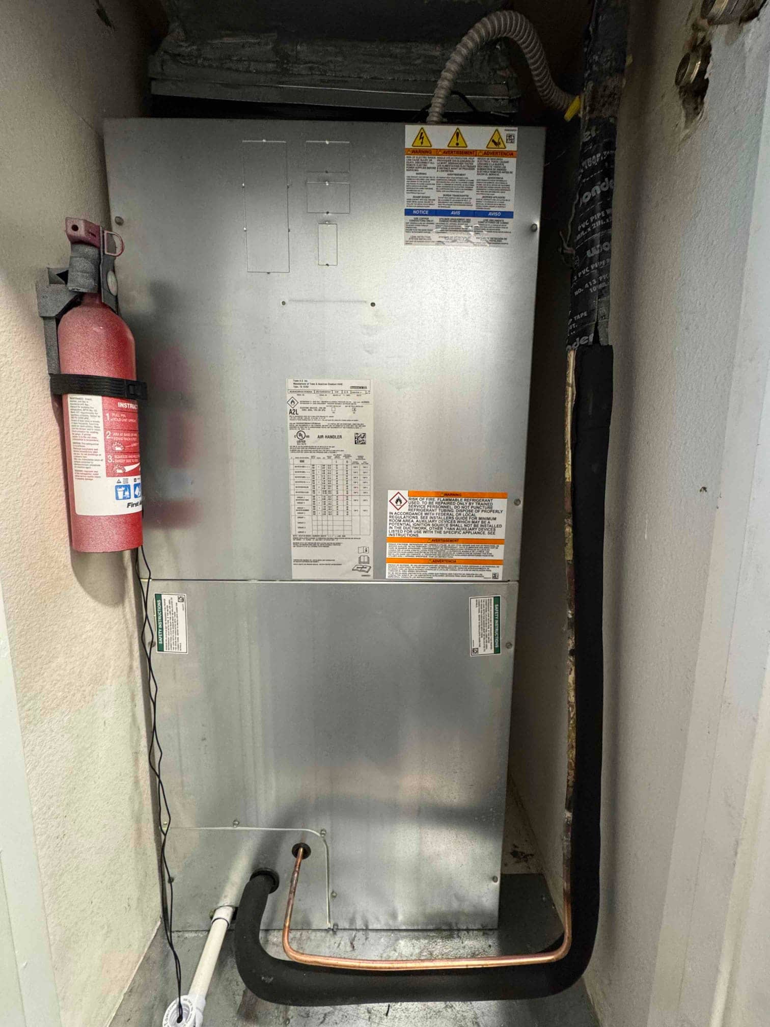 New indoor air handler installed in closet with insulated refrigerant lines and condensate drain connected on the drain pan.