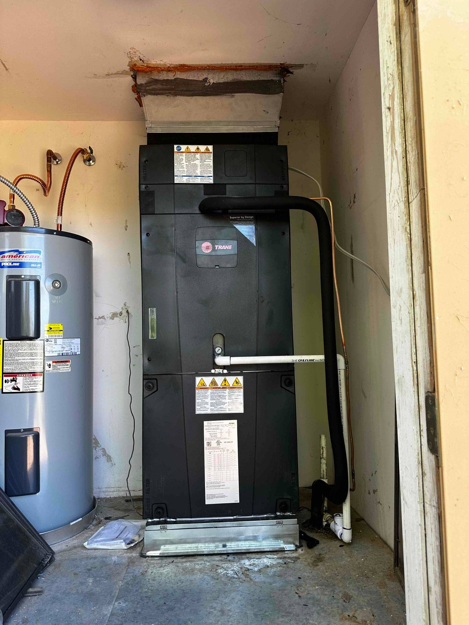 New indoor air handler installed on a stand with insulated refrigerant line and PVC condensate drain connected to the system.