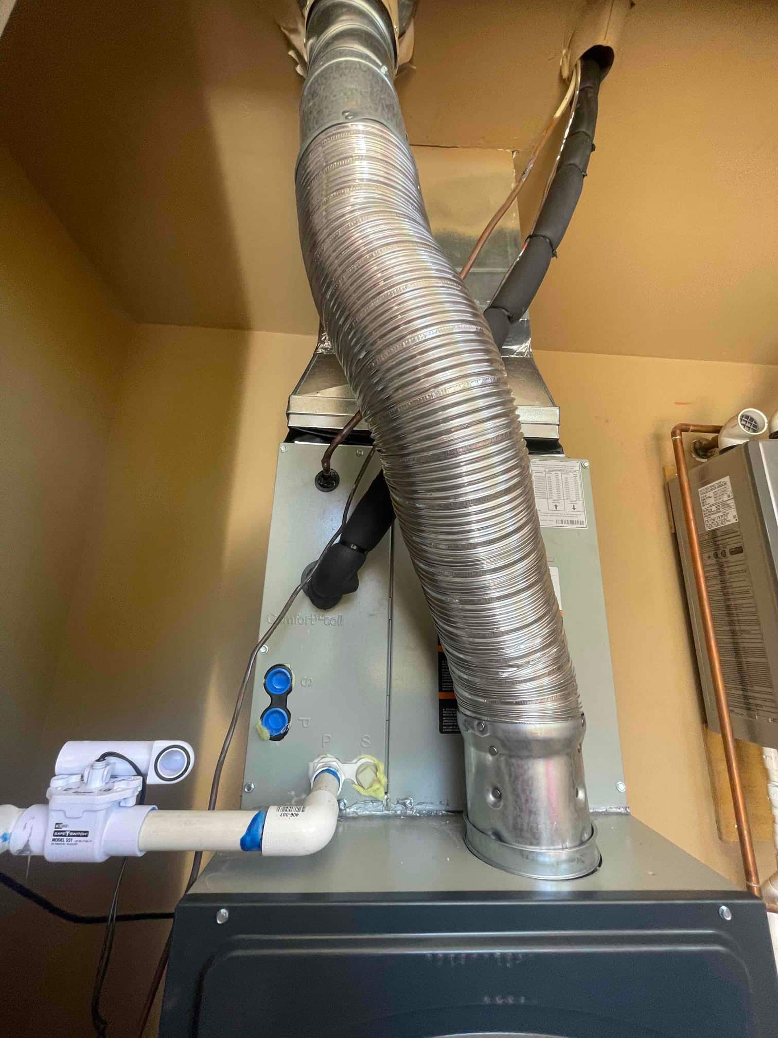 New indoor air handler with insulated refrigerant lines, condensate drain assembly, and metal duct connections sealed at the plenum.