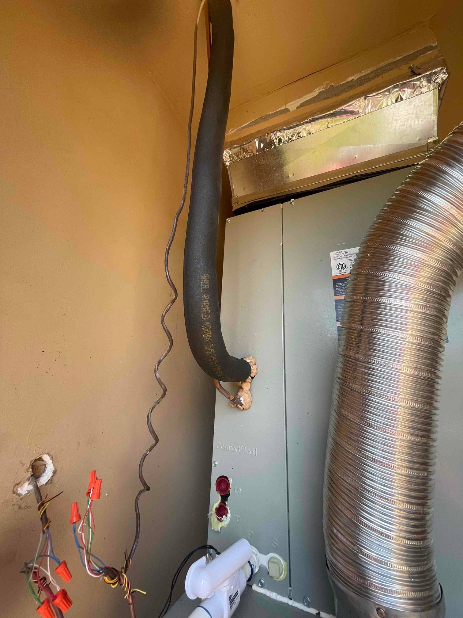 New indoor coil cabinet with insulated suction line, sealed refrigerant penetrations, drain assembly, and connected flexible duct in the equipment closet.
