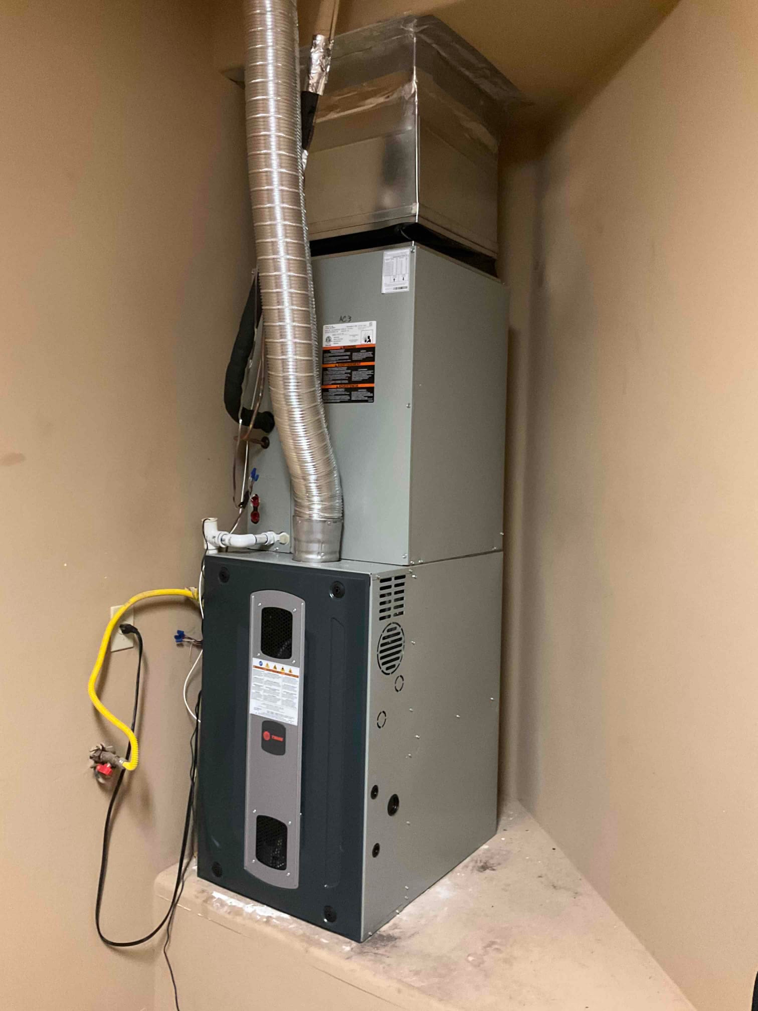 New indoor furnace and coil assembly installed with connected ductwork, condensate drain, gas line, and venting in a utility alcove.